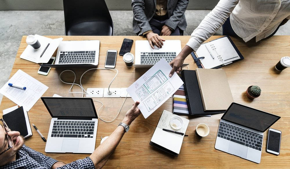 商業 桌布 壁紙 — Overhead view of four professionals collaborating around a wooden table with laptops notebooks and coffee cups.