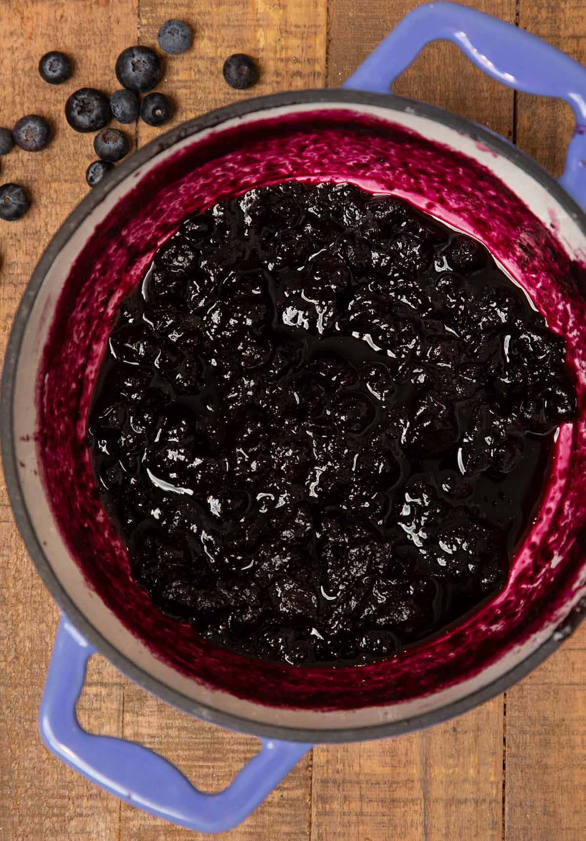 Blueberry Jam 桌布 壁紙 — Overhead view of glossy dark blueberry compote in a blue enamel pot on a rustic wooden surface.
