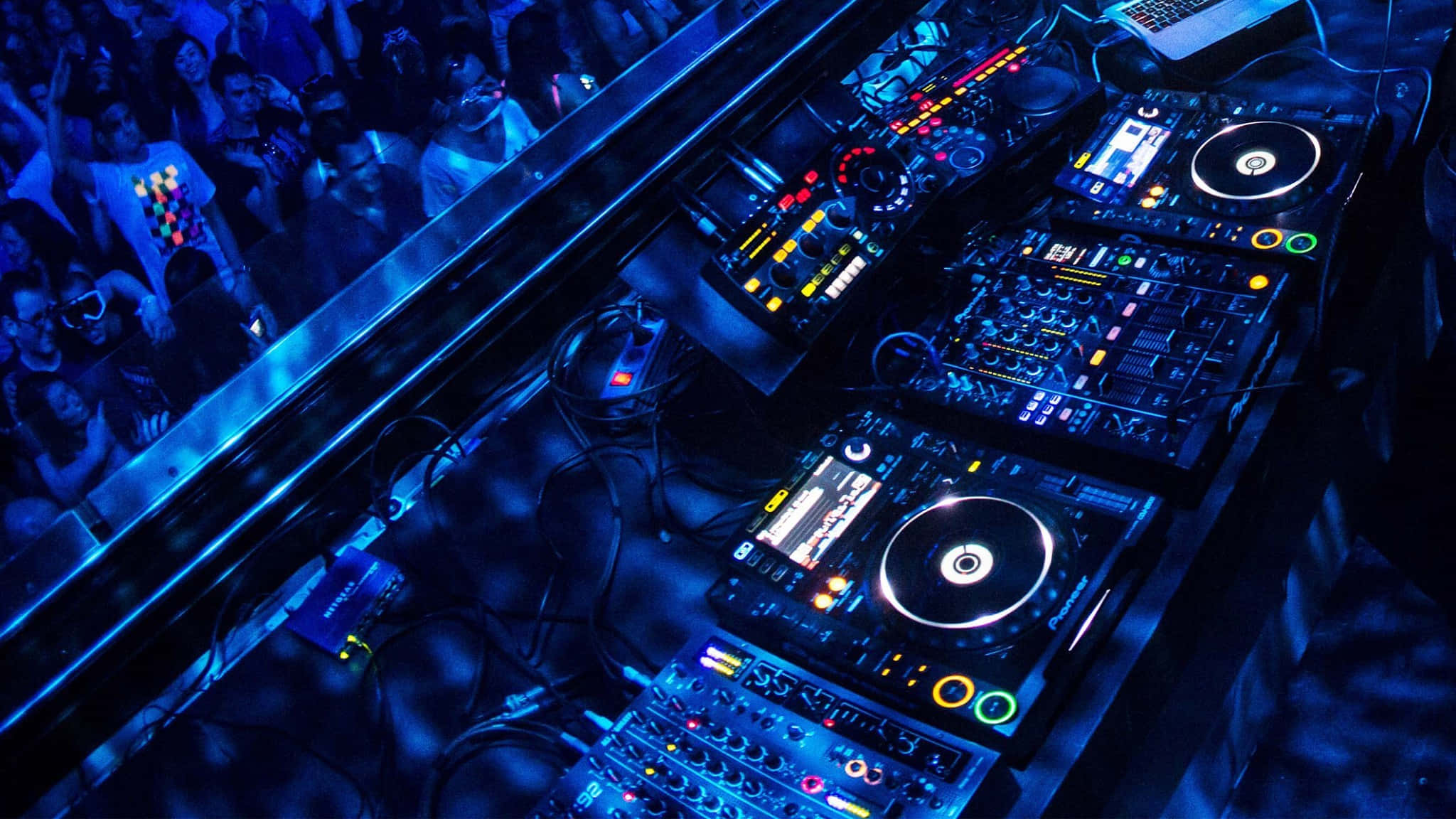 Dj Set 桌布 壁紙 — Overhead view of glowing DJ equipment bathed in blue light with a crowd watching below.