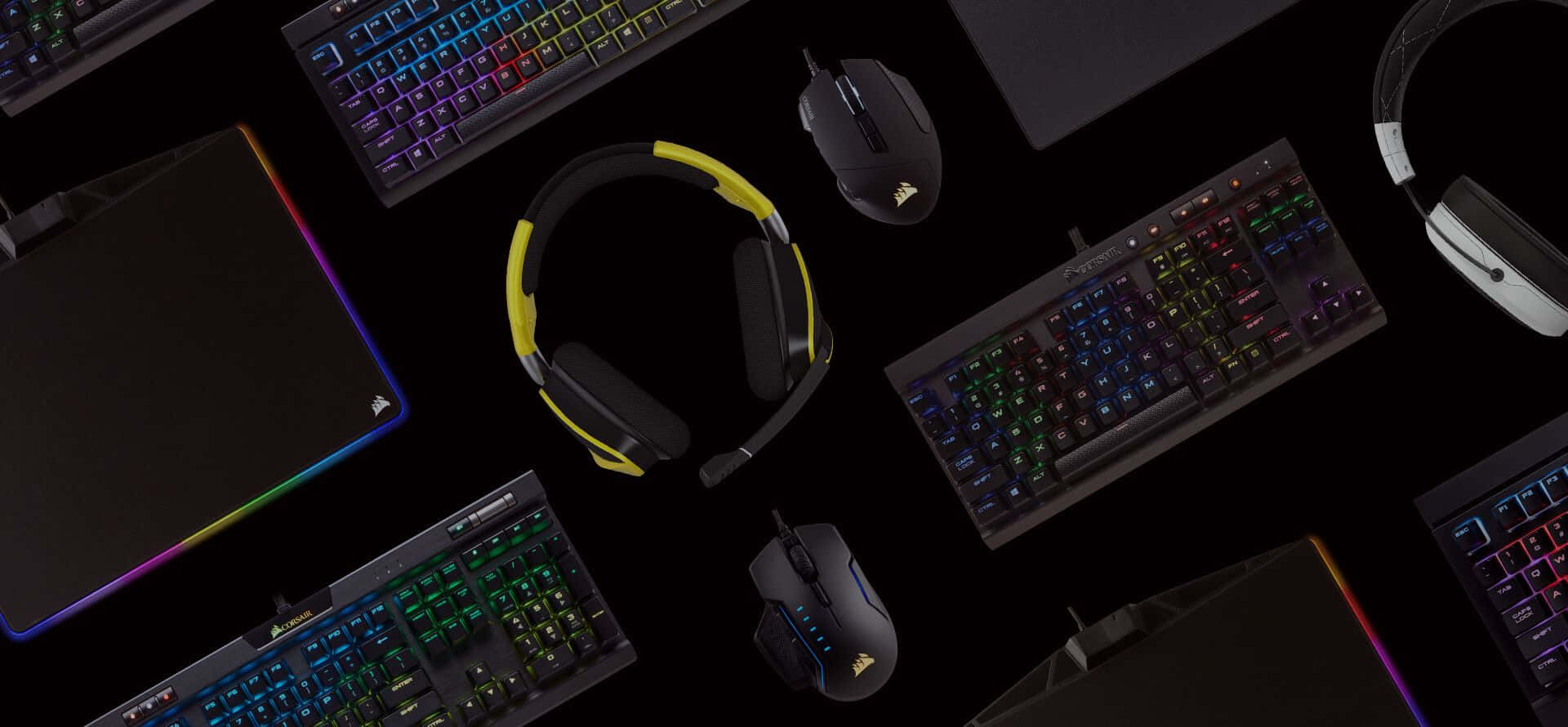 海盜船 桌布 壁紙 — Overhead view of glowing RGB keyboards mice and headphones arranged on a black surface showcasing gaming gear.