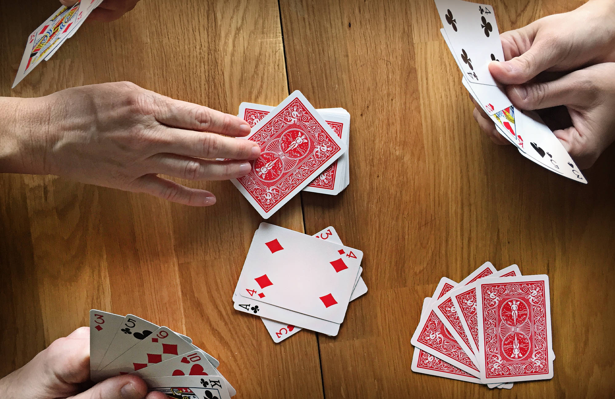 高清 桌布 壁紙 — Overhead view of hands dealing and holding playing cards on a warm wooden table during a game.