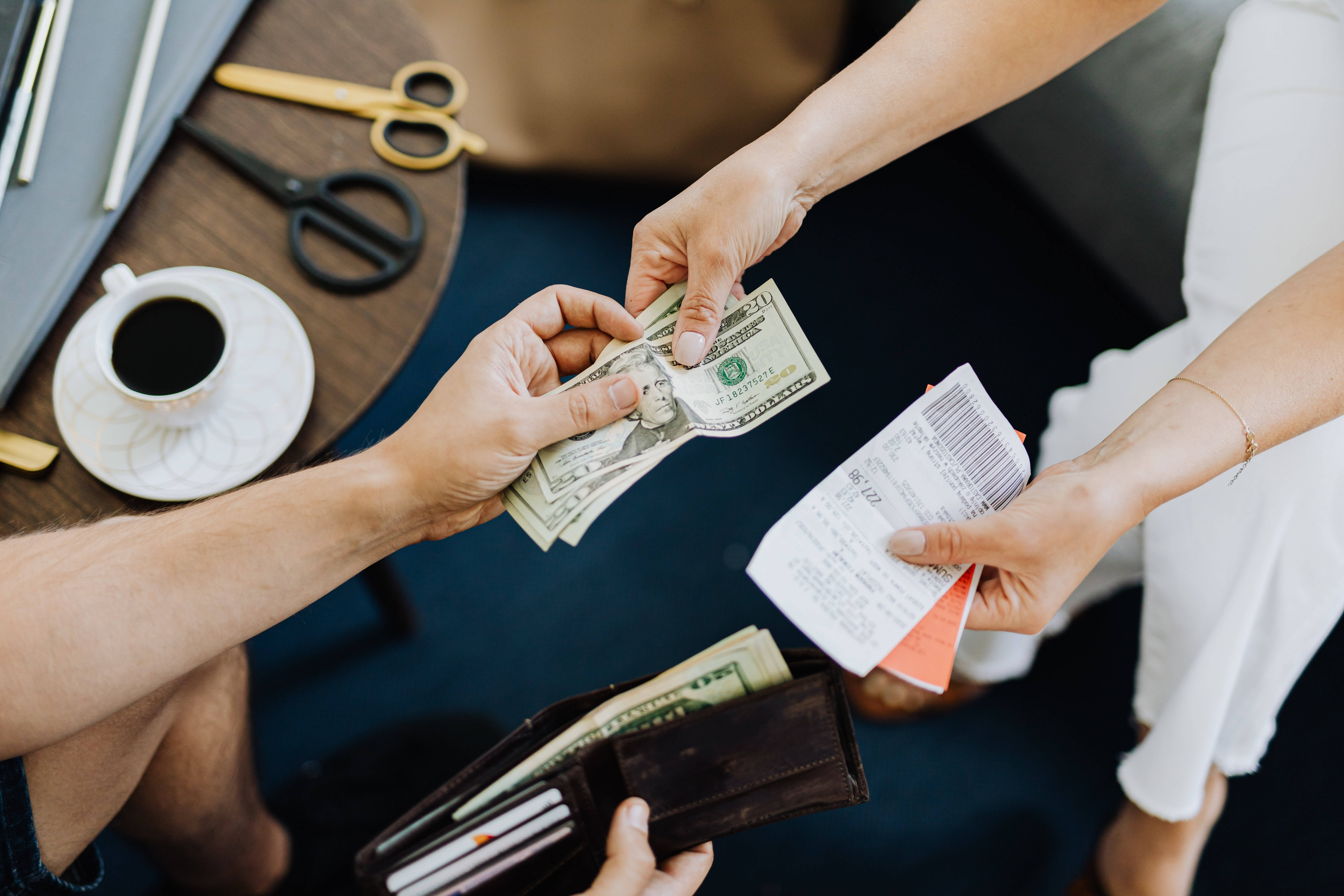 paper 桌布 壁紙 — Overhead view of hands exchanging cash and receipts at a wooden table with coffee and scissors nearby.