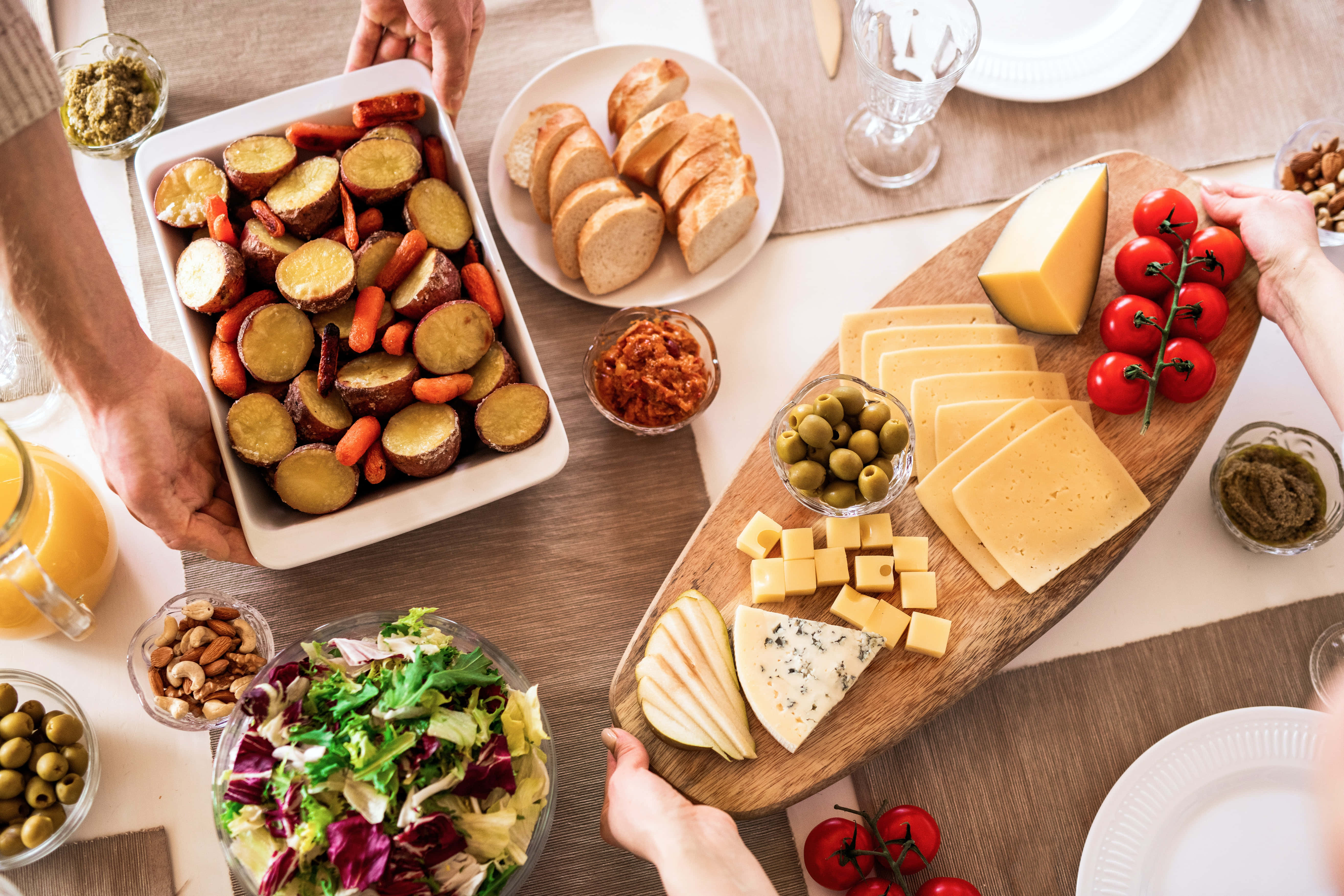 Cheese 桌布 壁紙 — Overhead view of hands serving a rustic charcuterie board with cheese bread salad and roasted veggies on a wooden table.