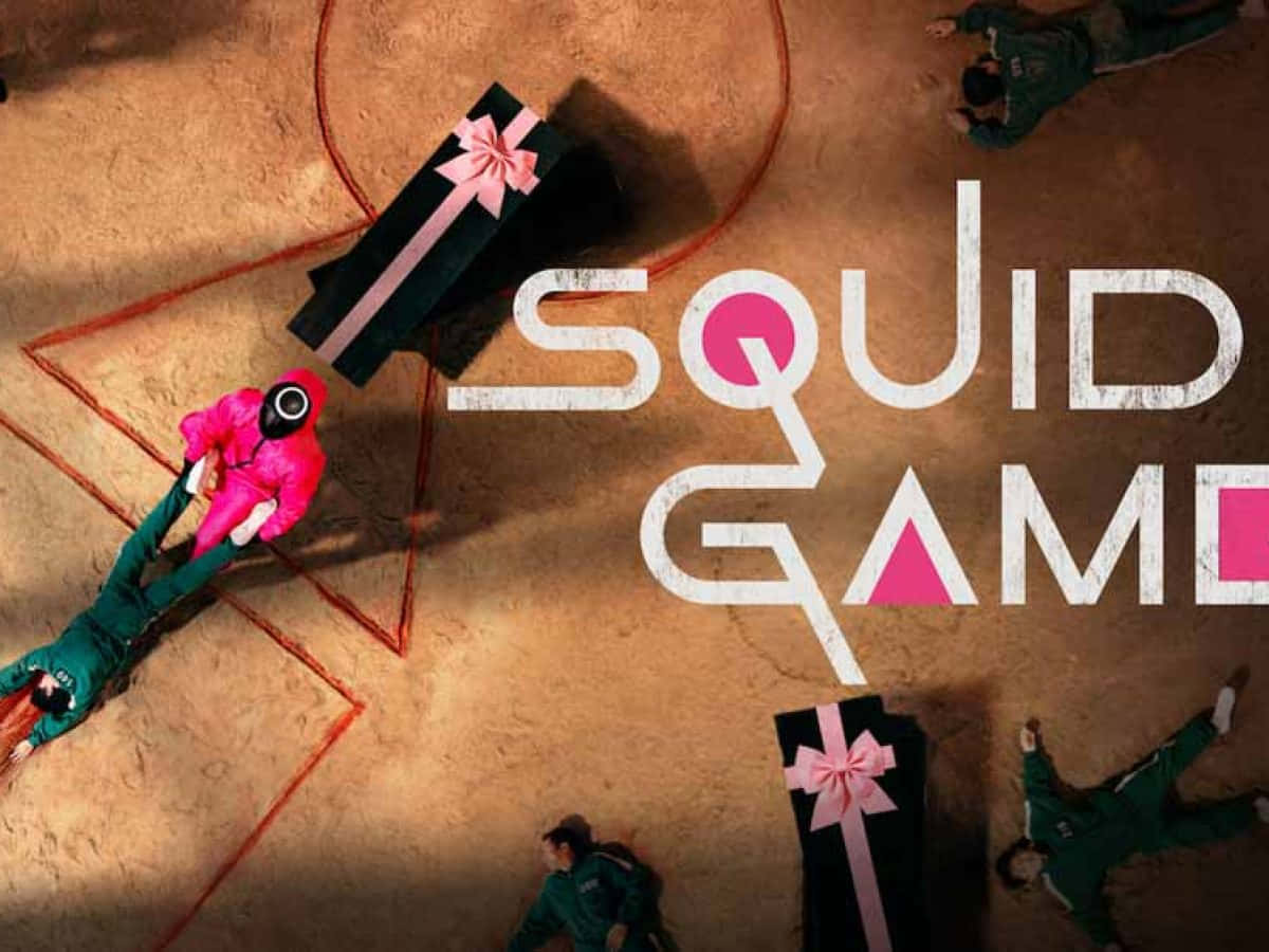 Squid Game 桌布 壁紙 — Overhead view of players in green and pink uniforms lying on dusty ground around giant gift boxes with pink ribbons.