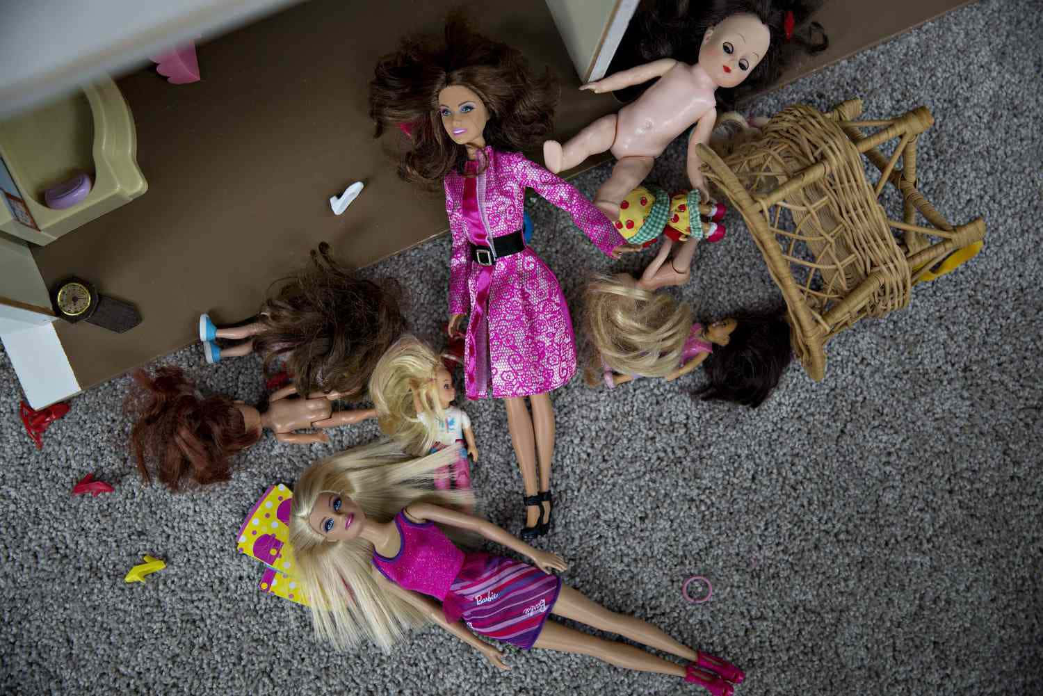 Barbie Doll 桌布 壁紙 — Overhead view of scattered dolls in colorful outfits lying on a gray carpet near a toppled wicker chair.
