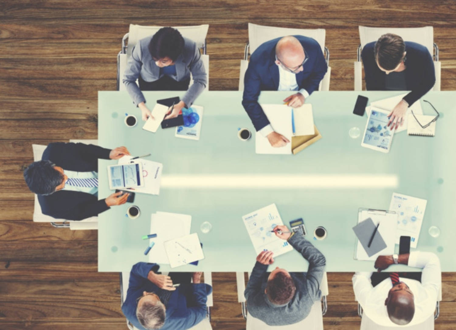 Working 桌布 壁紙 — Overhead view of six business professionals in suits collaborating around a glass conference table with documents and devices.