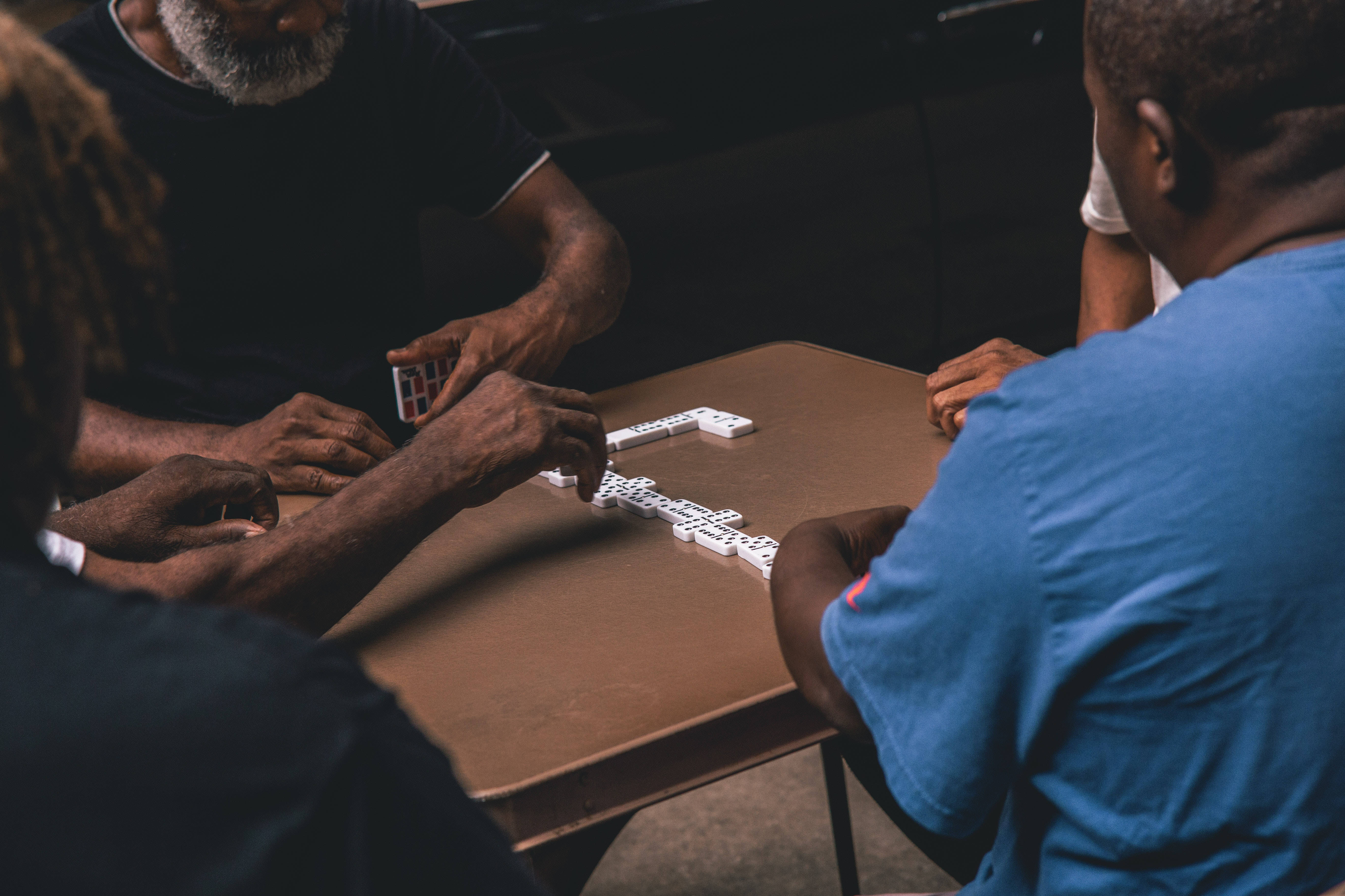 dominos 桌布 壁紙 — Overhead view of three men intensely playing dominoes around a wooden table in a dimly lit room.