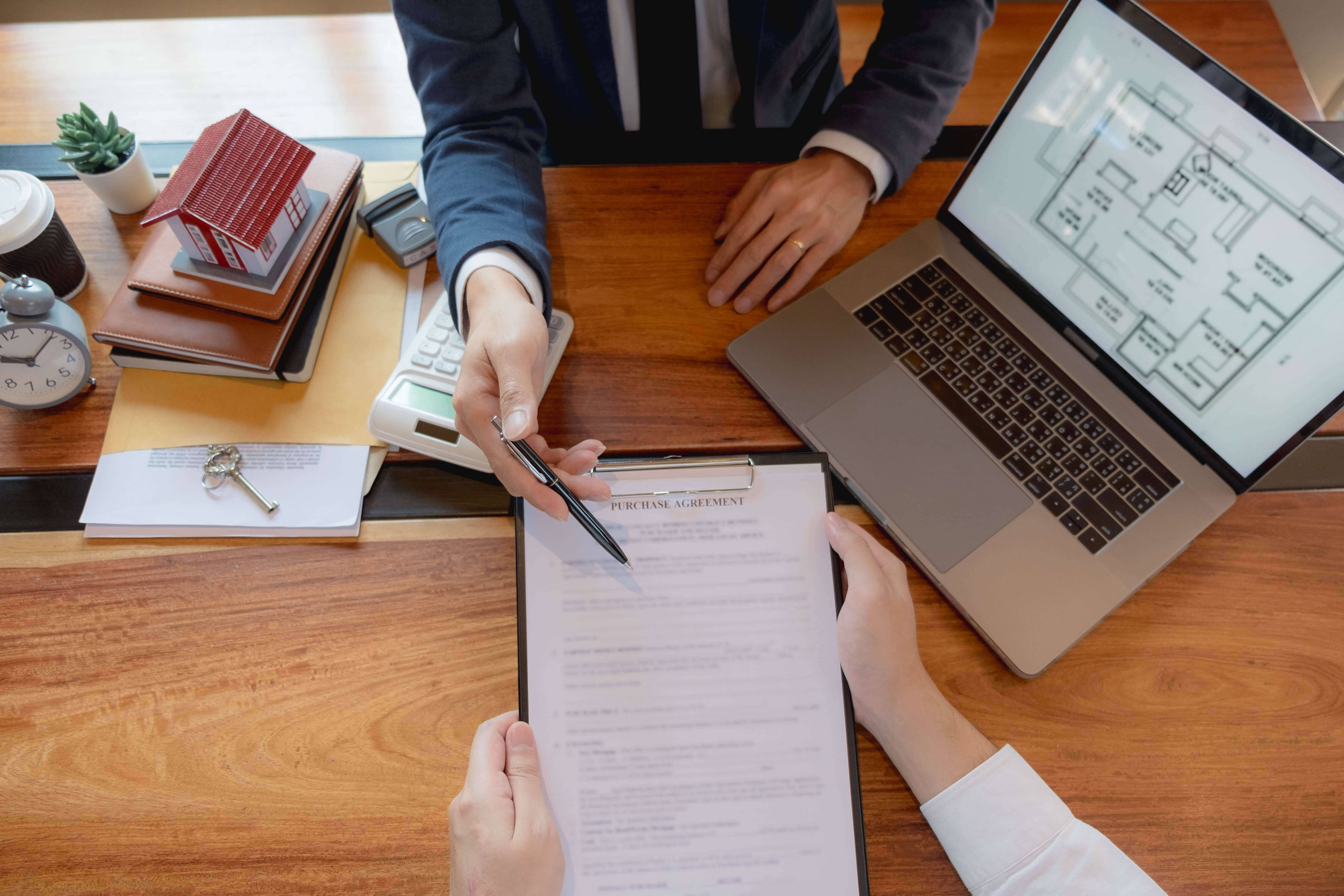 Work 桌布 壁紙 — Overhead view of two people signing a purchase agreement at a wooden desk with laptop floor plan and real estate props.