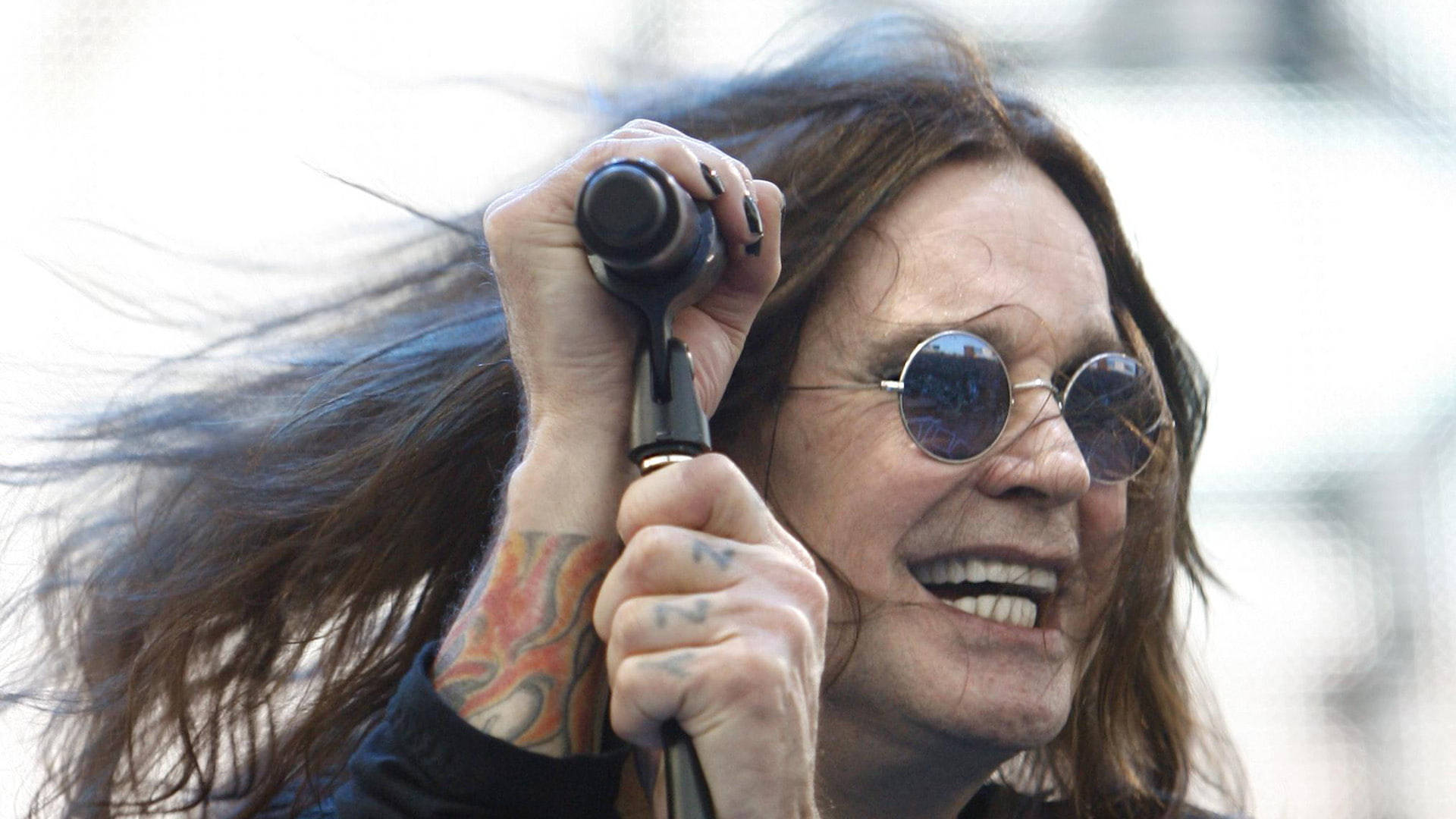 Ozzy Osbourne 桌布 壁紙 — Ozzy Osbourne 咧嘴大笑，緊握麥克風，長髮隨風飄揚。