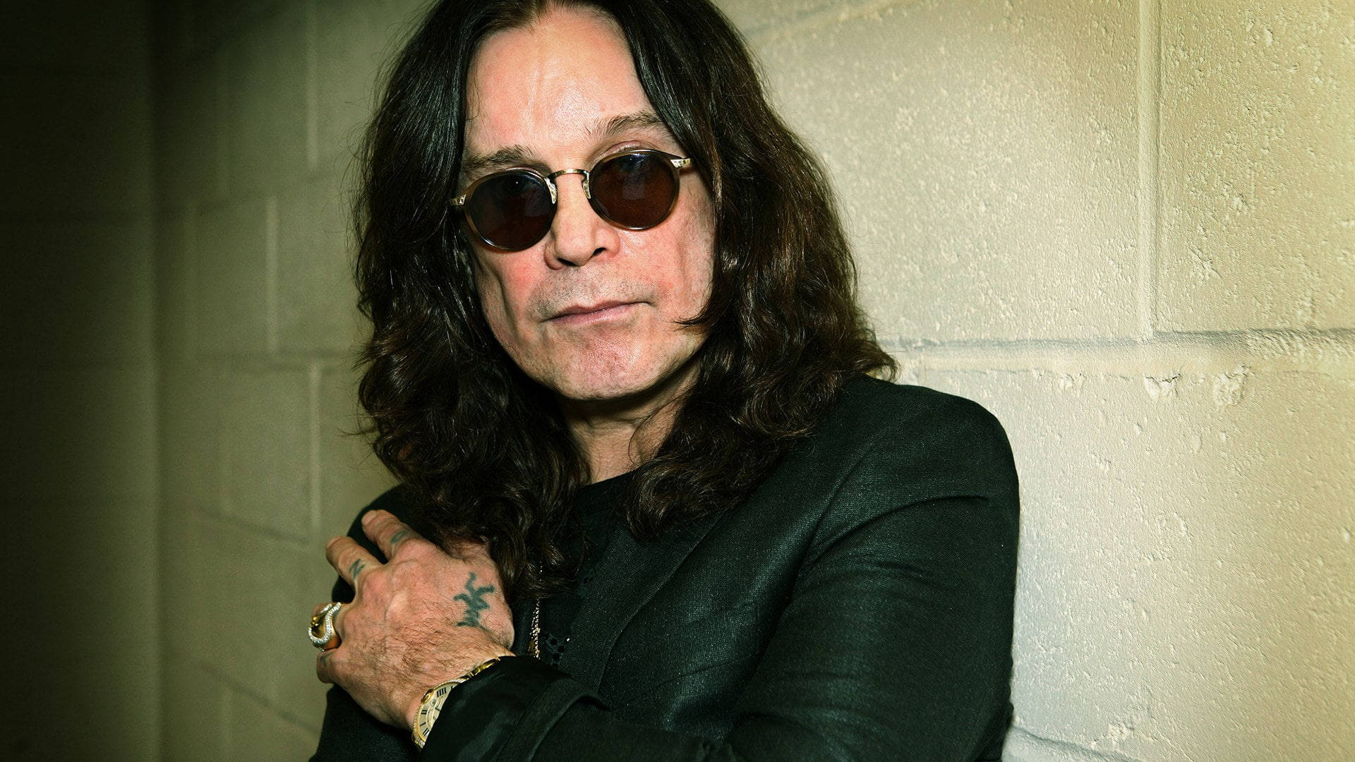 Ozzy Osbourne 桌布 壁紙 — Ozzy Osbourne 戴著太陽眼鏡和黑色外套靠在混凝土牆上，手上的刺青清晰可見。