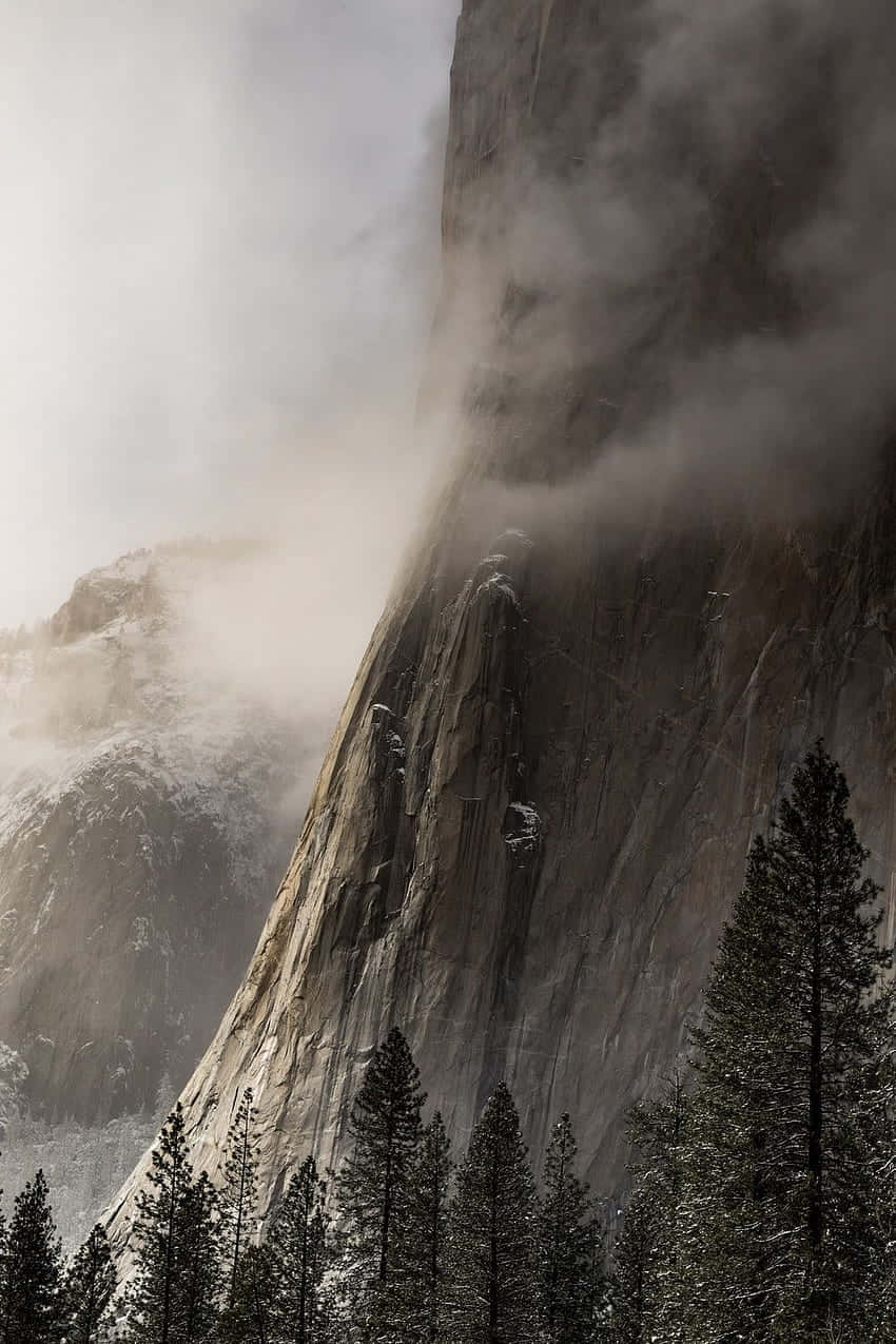  壁紙 — 攀岩者攀登霧氣籠罩的花崗岩峭壁，雪花灑落在山峰和下方的常青樹上。
