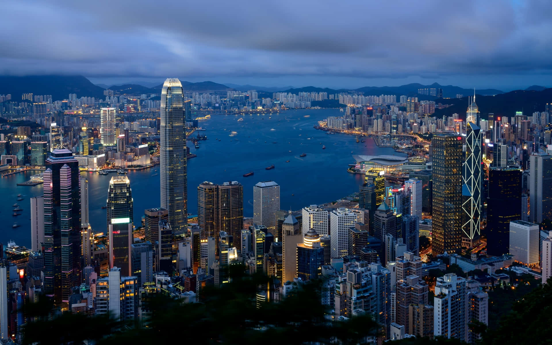 黃昏時分的香港城市景觀，燈火通明的摩天大樓和港口。 — Macbook Pro 壁紙