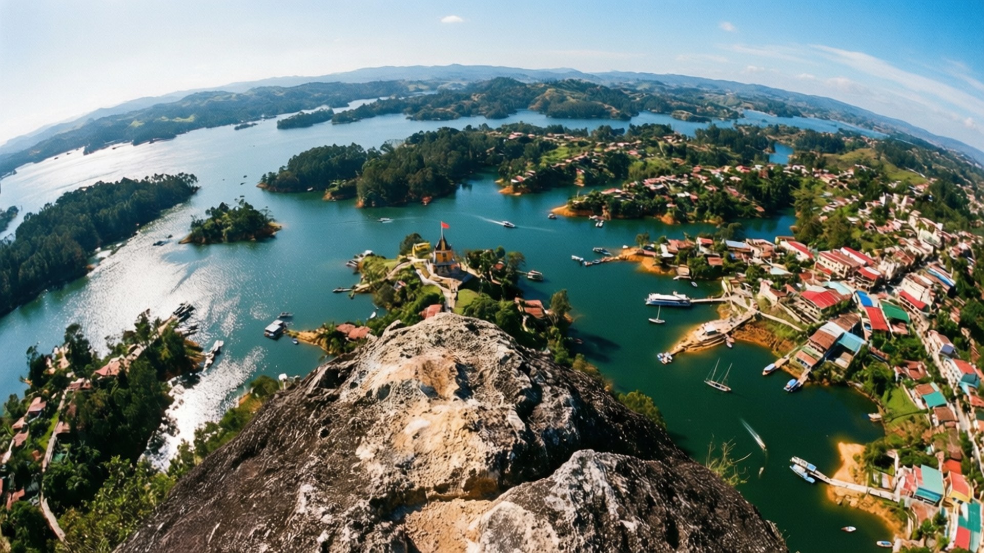 Peñol's Panorama 壁紙 — 從岩石懸崖俯瞰碧綠湖泊的全景，湖中點綴著島嶼和色彩繽紛的村莊房屋。