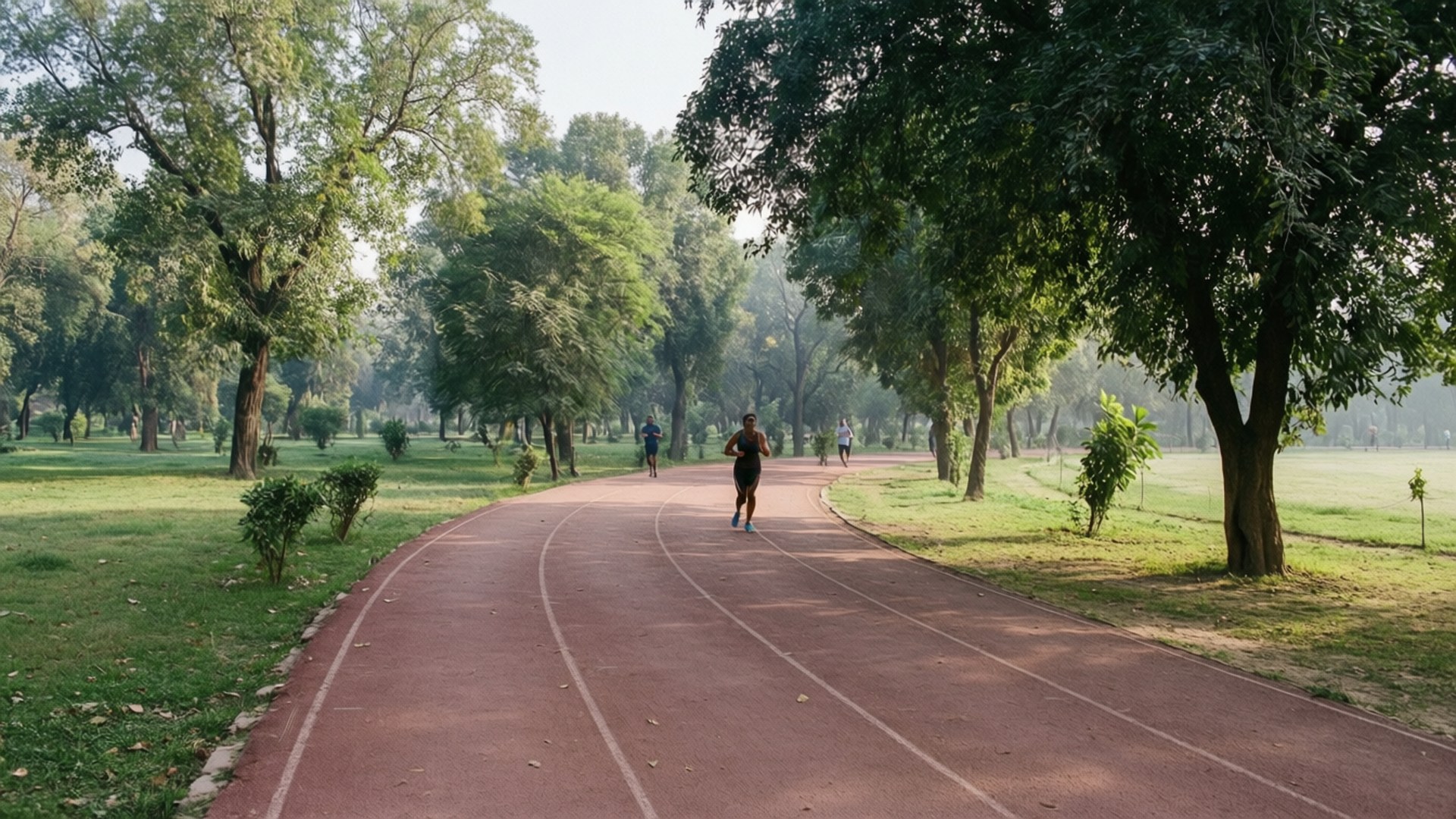 Race Course Park Morning 壁紙 — 一名穿著黑色短褲和藍色鞋子的跑者，在陽光燦爛下，於一條彎曲的紅色跑道上衝刺，跑道兩旁是茂密的綠樹和草地。