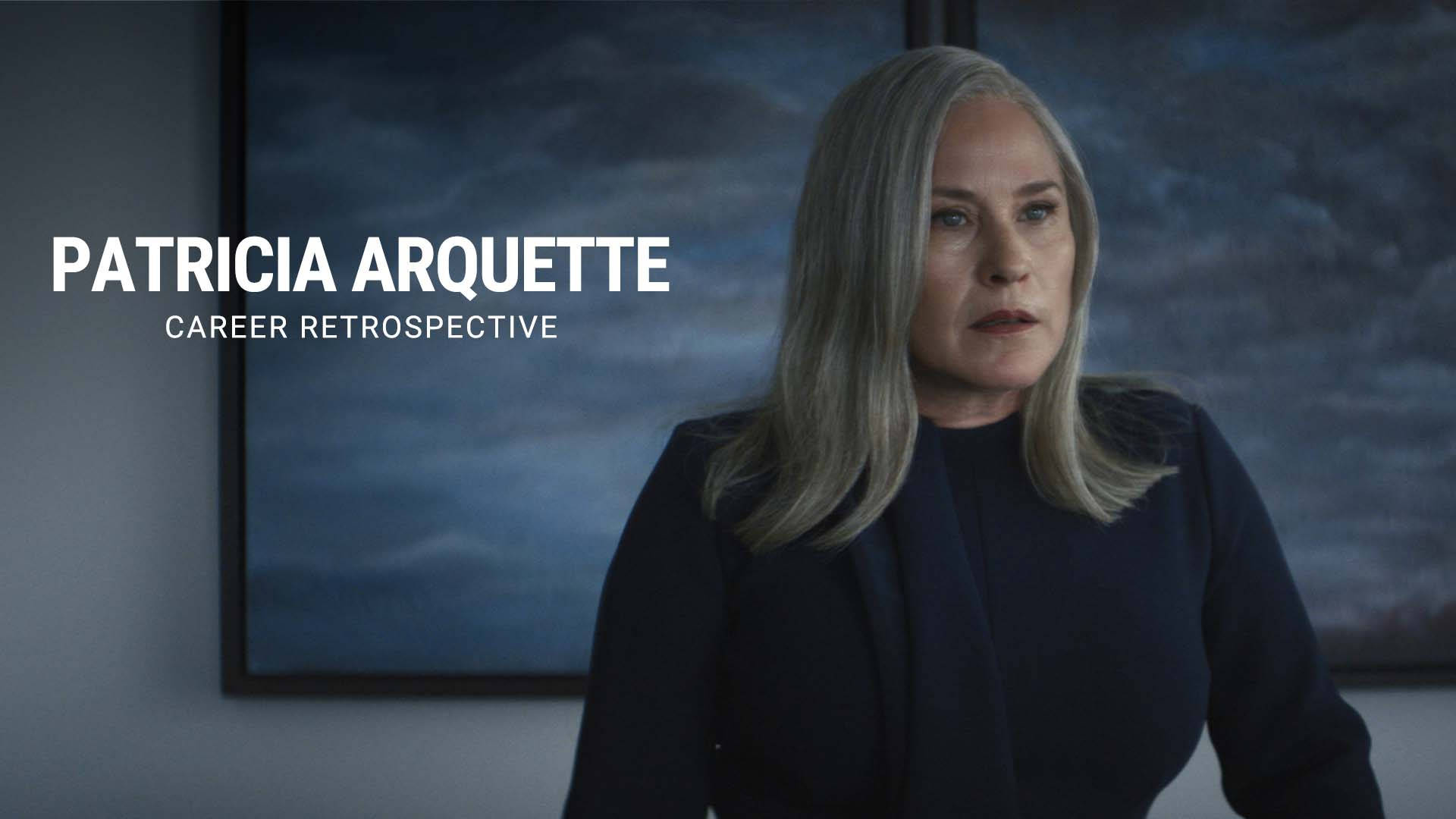電影動圖 桌布 壁紙 — Patricia Arquette 站在昏暗的房間裡，穿著深色西裝外套，身後有一幅陰沉多雲天空的畫。