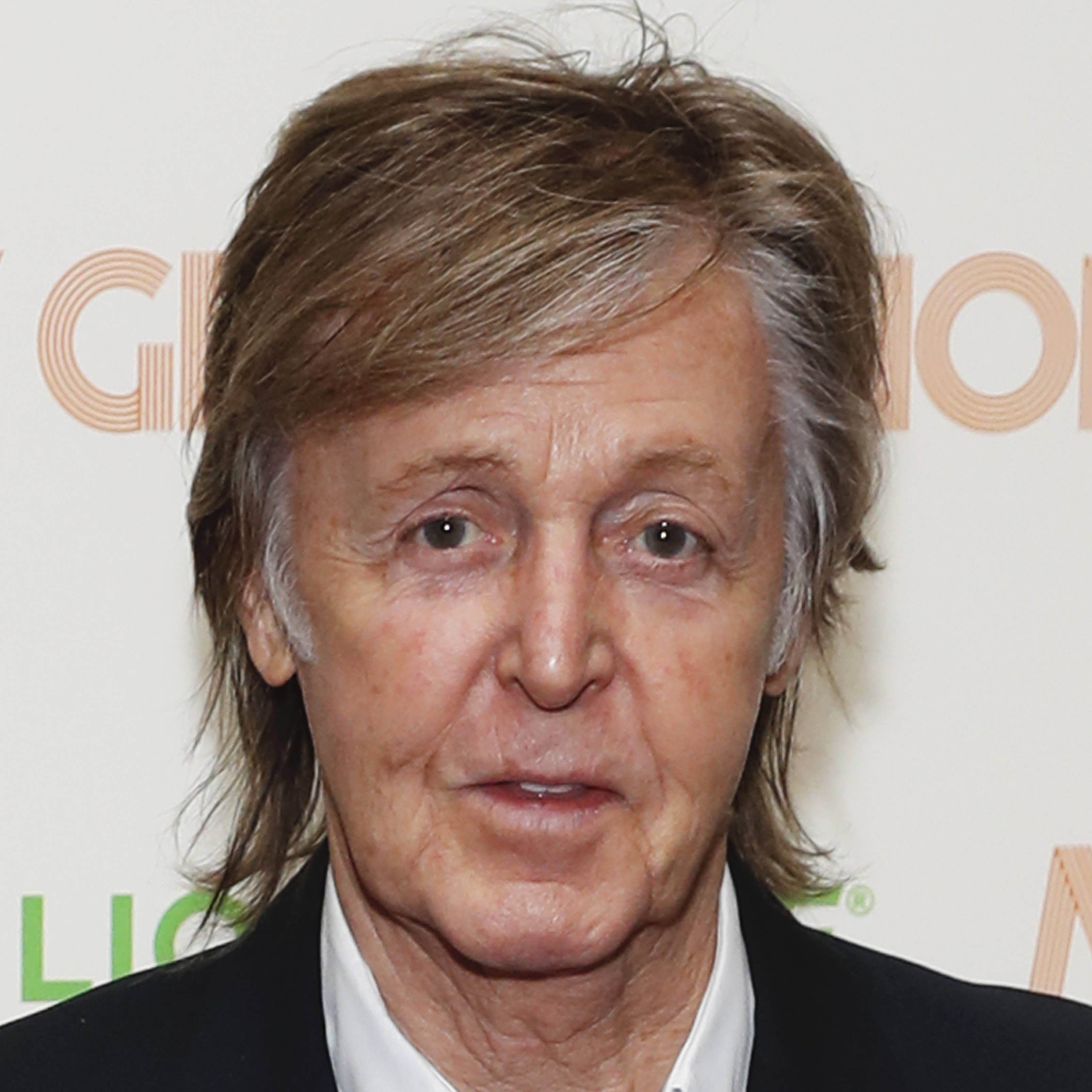 Celebrity 桌布 壁紙 — Paul McCartney 的特寫肖像，他有亂糟糟的棕色頭髮和灰色髮絲，穿著黑色西裝和白色襯衫，背景是有品牌標誌的。