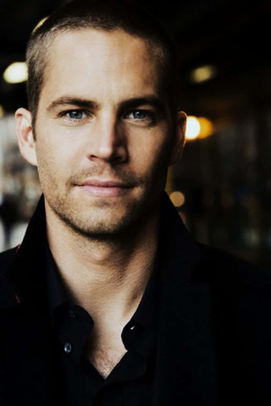 Paul Walker 桌布 壁紙 — Paul Walker 身穿黑色襯衫，背景帶有柔和散景燈光的特寫肖像。