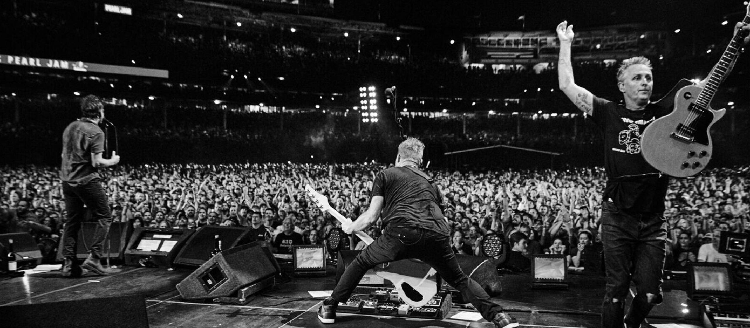 concert 桌布 壁紙 — Pearl Jam 樂團成員在夜間於舞台上，在大量歡呼的群眾面前充滿活力地表演的黑白演唱會照片。