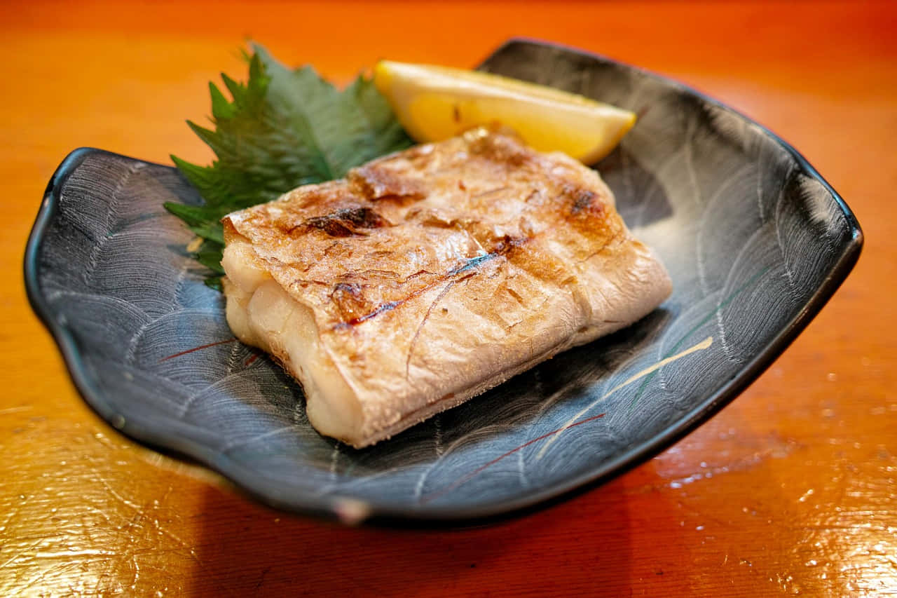  壁紙 — 完美烤魚片，魚皮焦脆，放在深色陶瓷盤上，旁邊有檸檬角和綠葉。