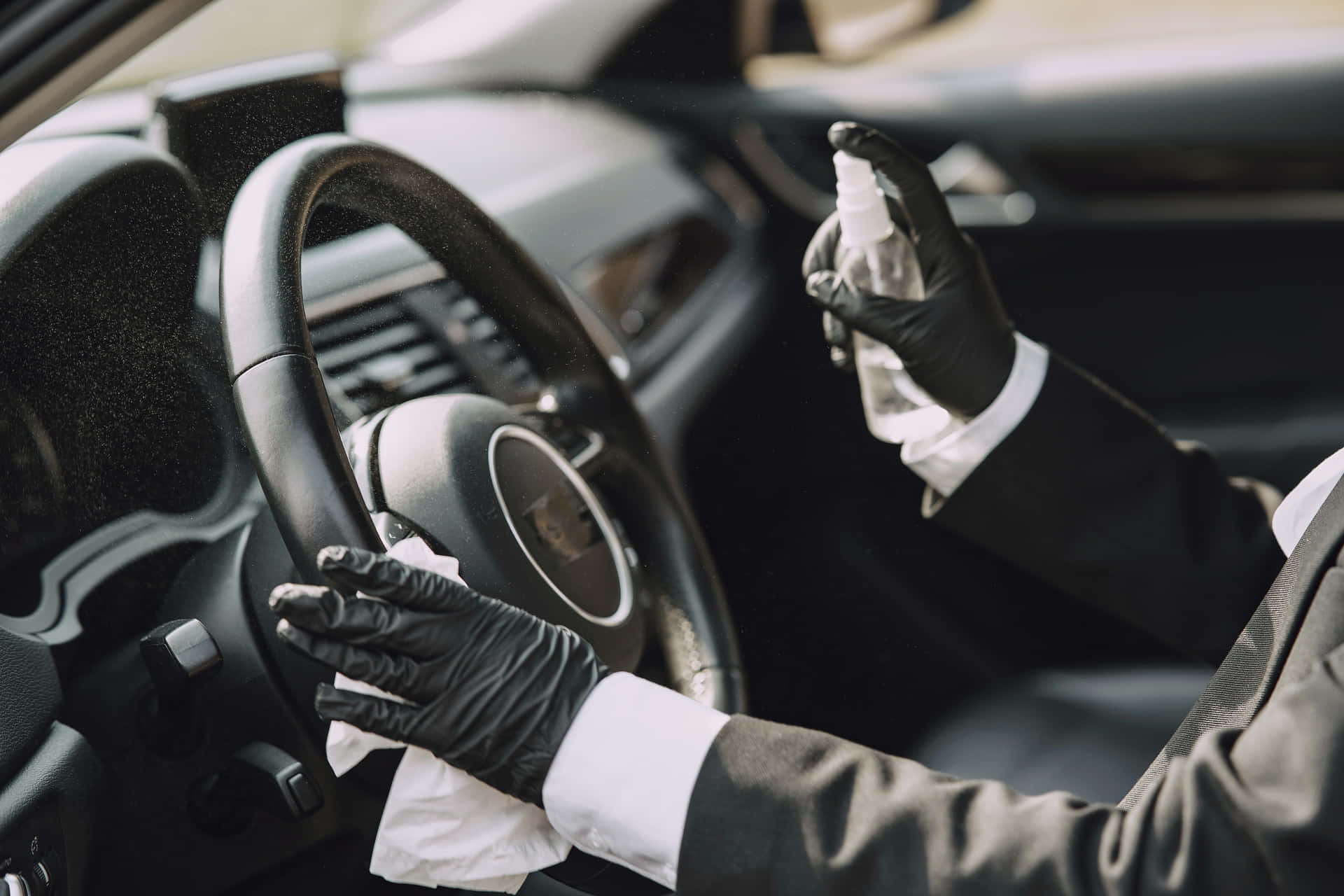 穿西裝和手套的人用噴霧和布消毒汽車方向盤。 — 車內 壁紙