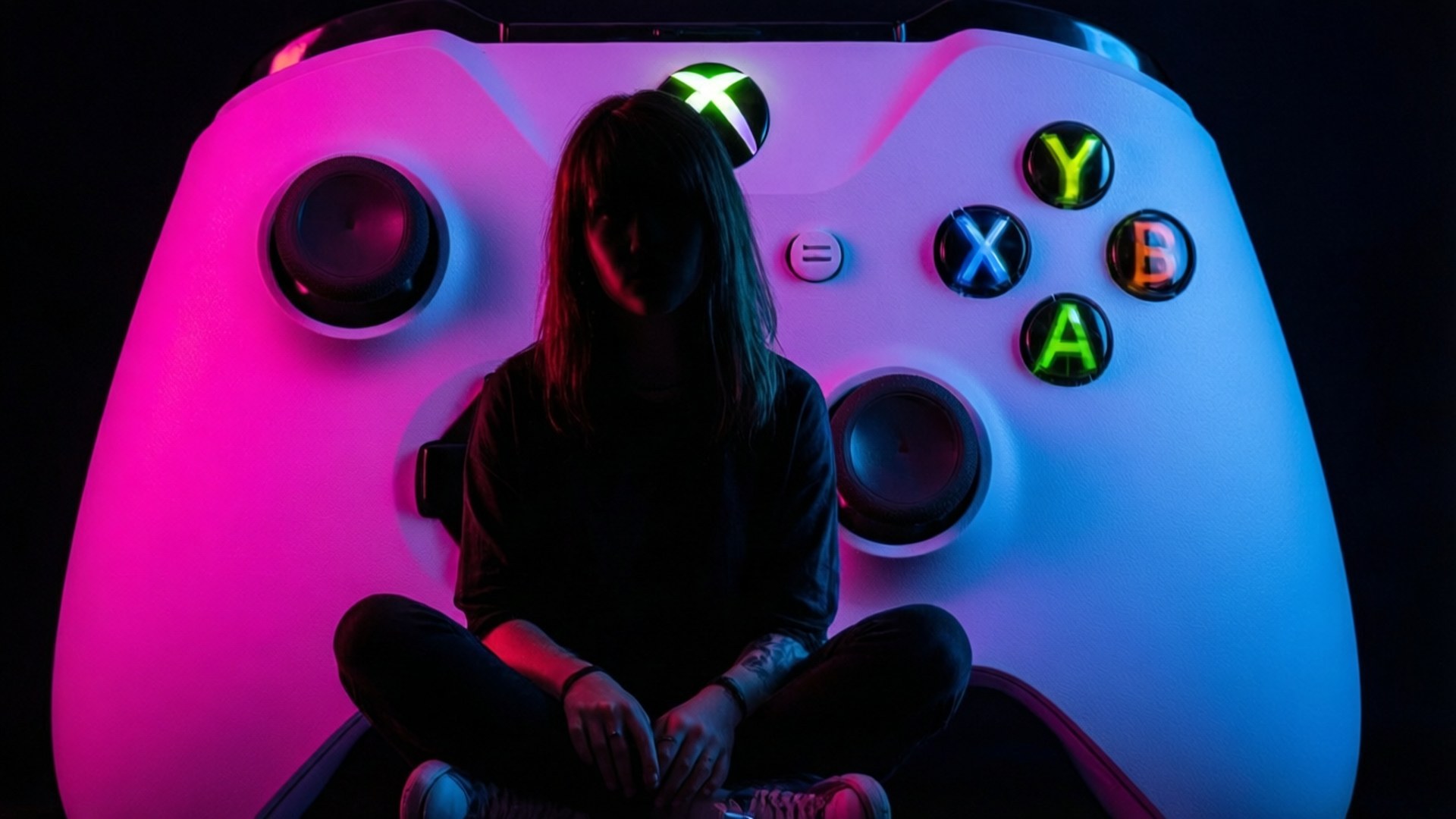 Gamer Girl with Xbox 壁紙 — 一個人以剪影形式坐在一個巨大的發光Xbox控制器內，沐浴在粉紅色和藍色的霓虹燈光中。