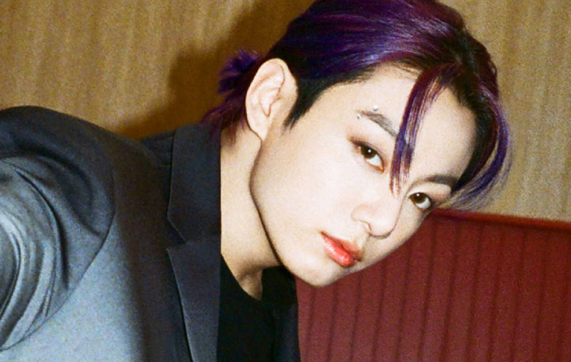 擁有紫色頭髮和紅唇的人穿著深色西裝，凝視著相機。 — Jungkook 壁紙