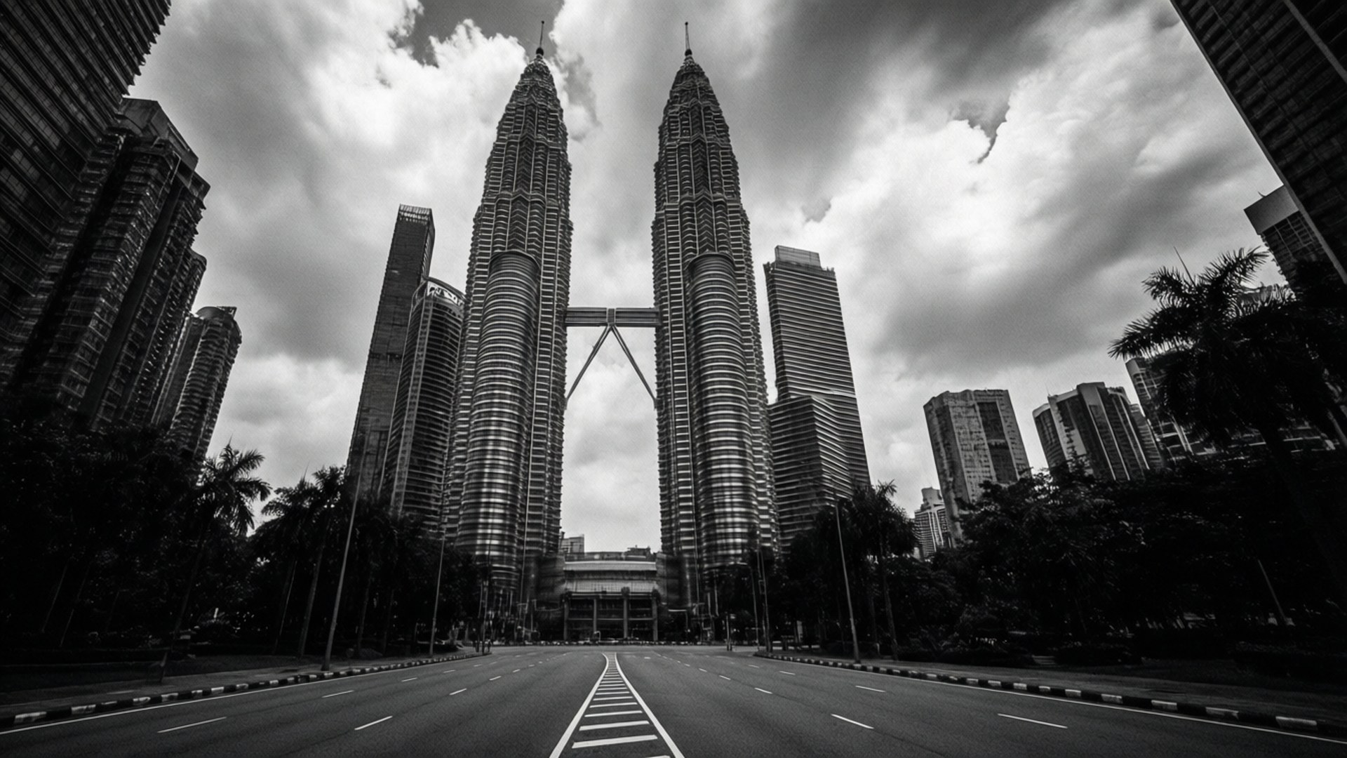 Monochrome Giants 壁紙 — 一張戲劇性的低角度黑白照片，展示雙子星塔被寬闊空蕩的道路和陰天天空所環繞。