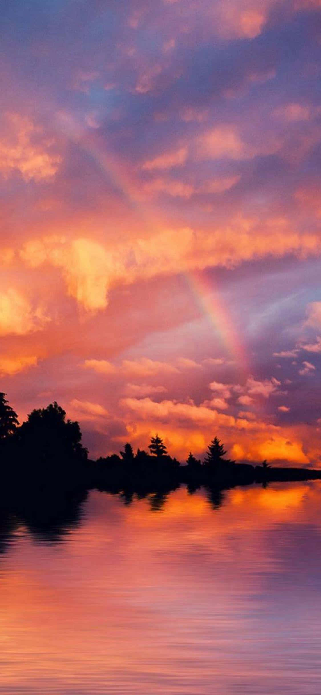 Colorful Sunset 桌布 壁紙 — 平靜的湖面上夕陽燦爛，彩虹穿過火橙色和紫色的雲彩，倒映在水中。