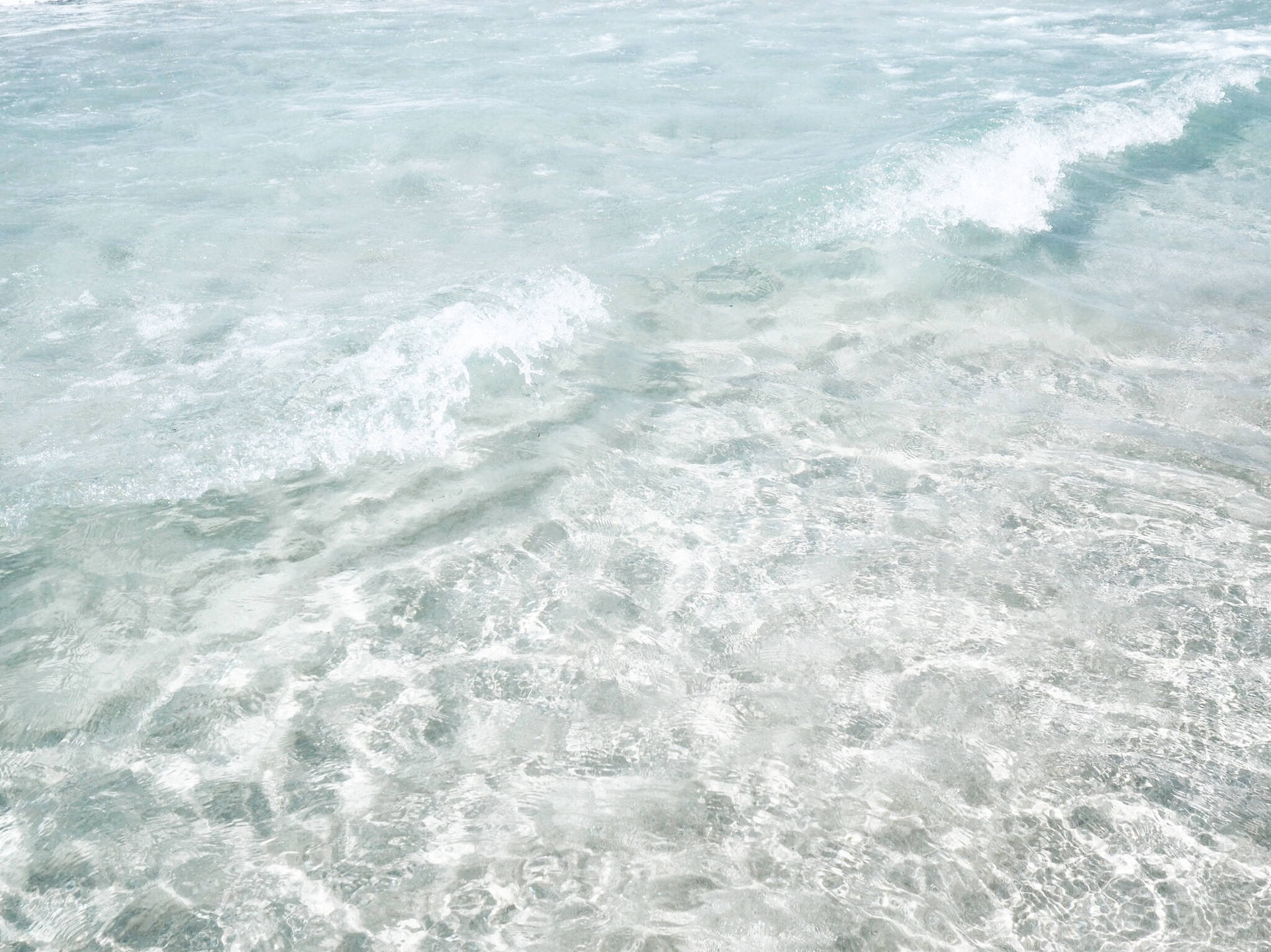 清澈藍綠色海水中翻滾著白色泡沫的溫柔海浪。 — Pastel 壁紙