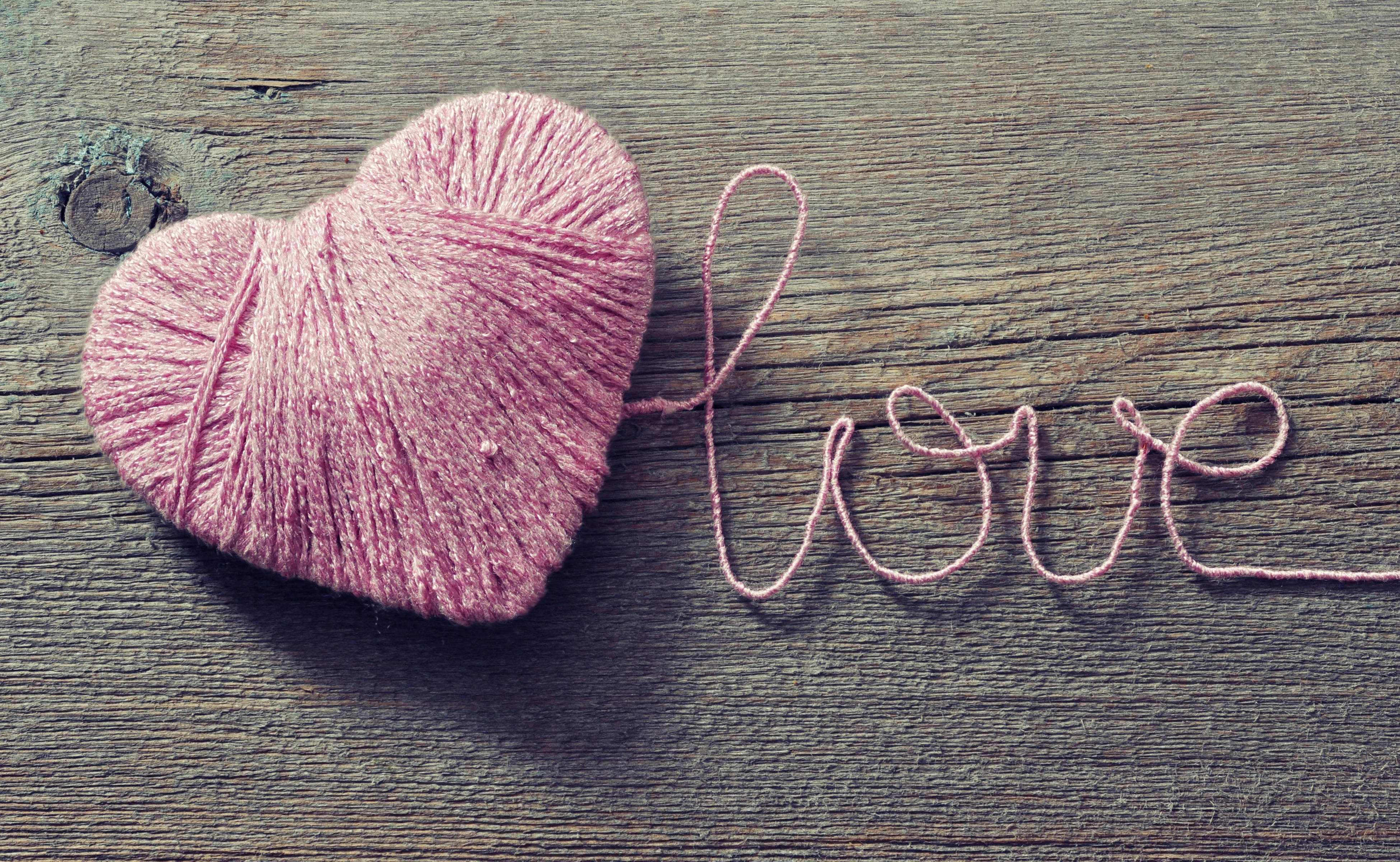 愛心 桌布 壁紙 — 一個粉紅色毛線心形和用毛線拼出的 love 字樣，放在一塊風化的木頭表面上。