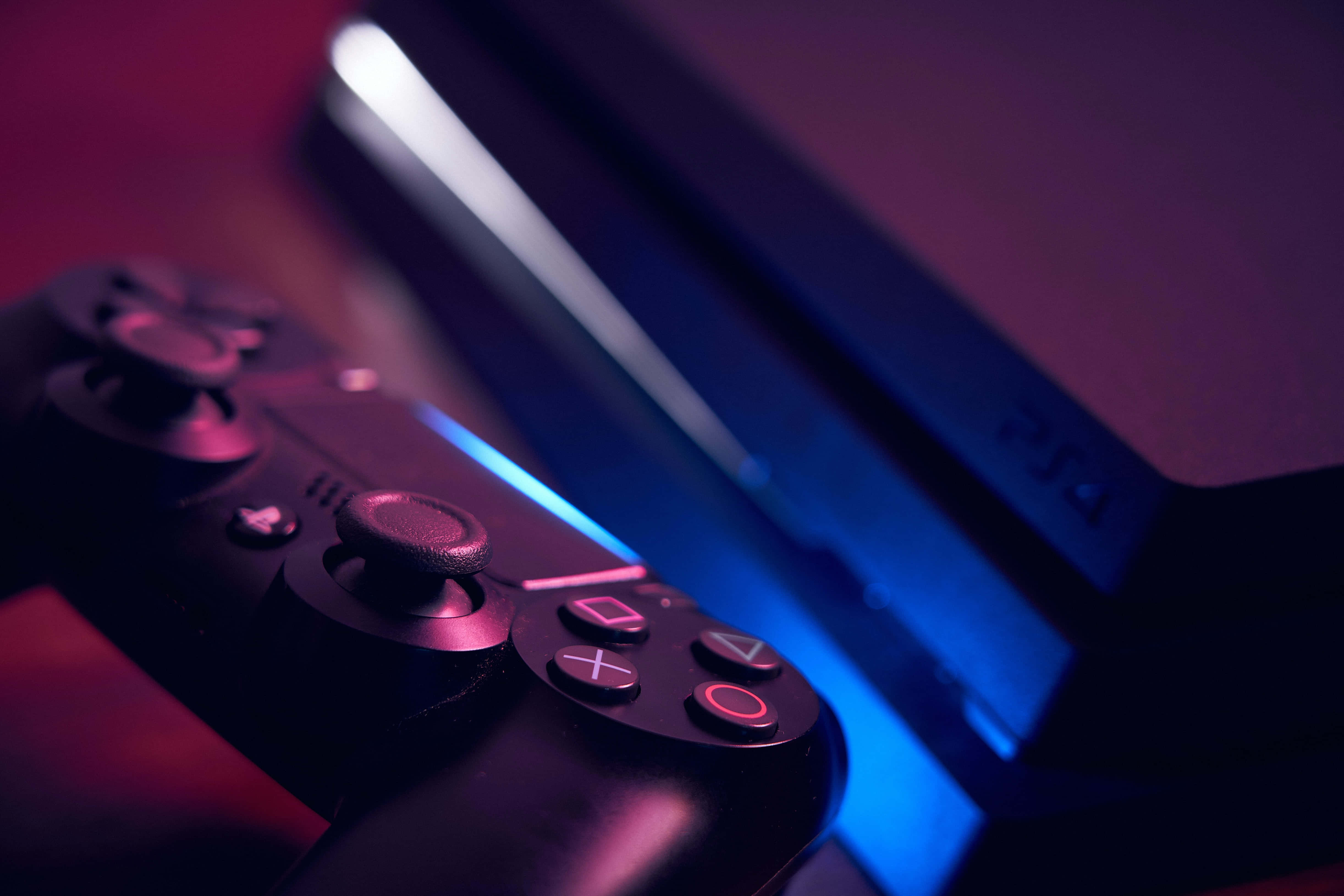 Gaming Consoles 桌布 壁紙 — PlayStation 4 控制器和主機的特寫，沐浴在鮮豔的紅色和藍色霓虹燈光中。