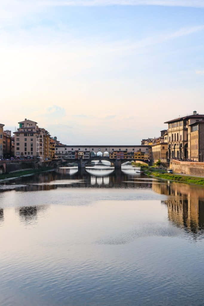 晴朗天空 桌布 壁紙 — Ponte Vecchio 橋靜靜地倒映在阿諾河中，金色時光的光芒沐浴著歷史悠久的佛羅倫斯建築。