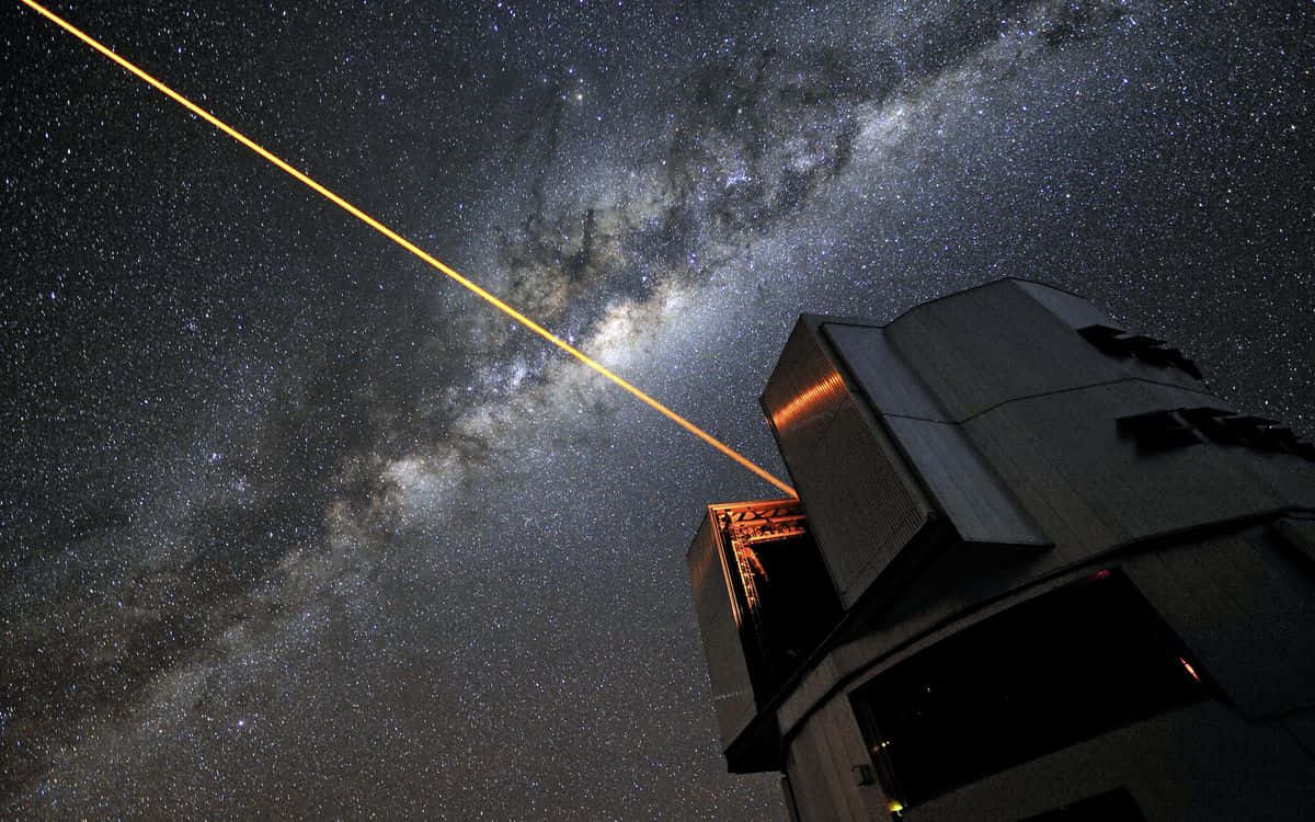  壁紙 — 一道強大的黃色雷射光束從望遠鏡射向佈滿銀河的星空夜空。