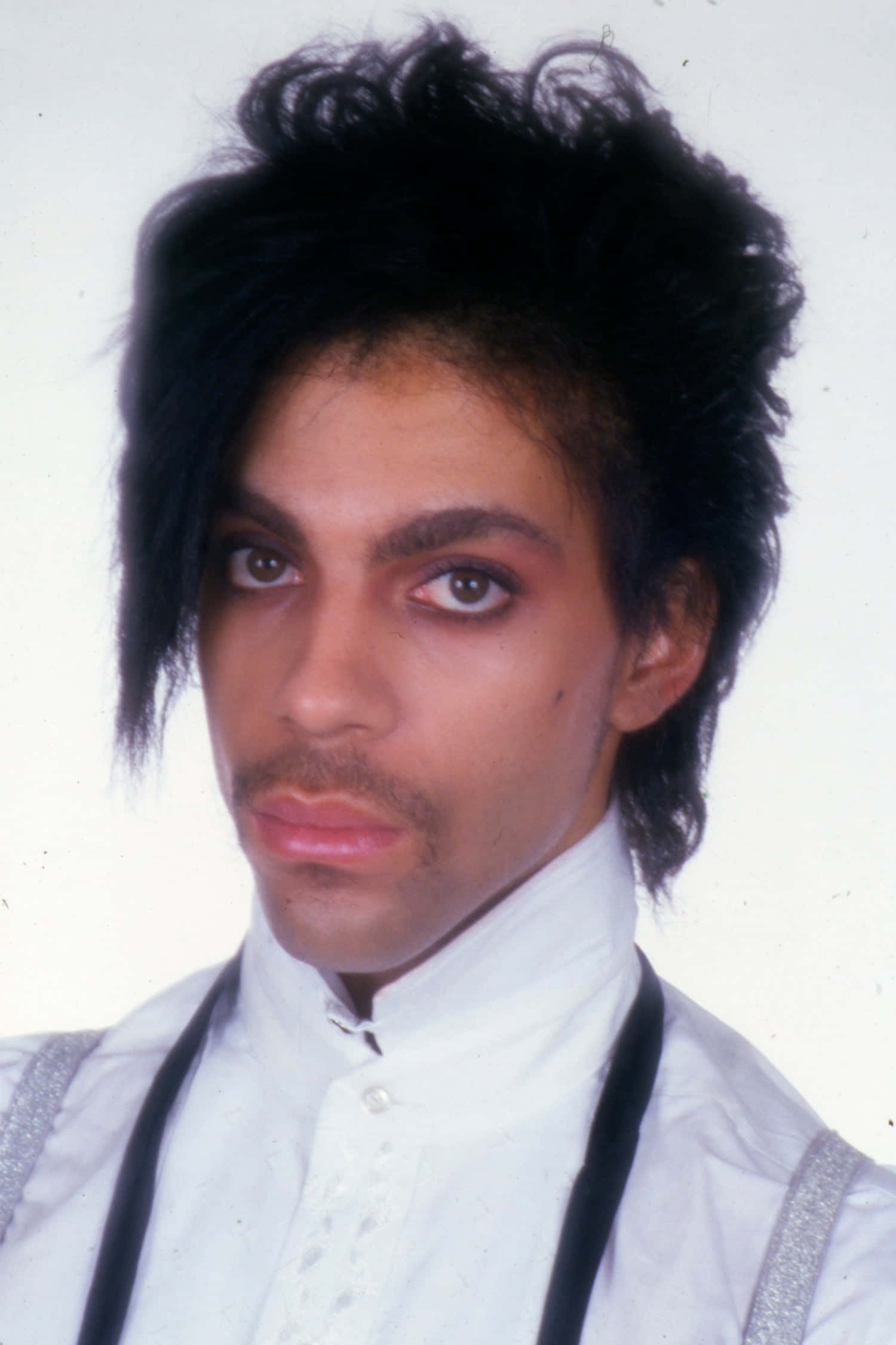 Prince 桌布 壁紙 — Prince 以戲劇性的眼妝和尖刺黑髮，在純白背景前凝視。