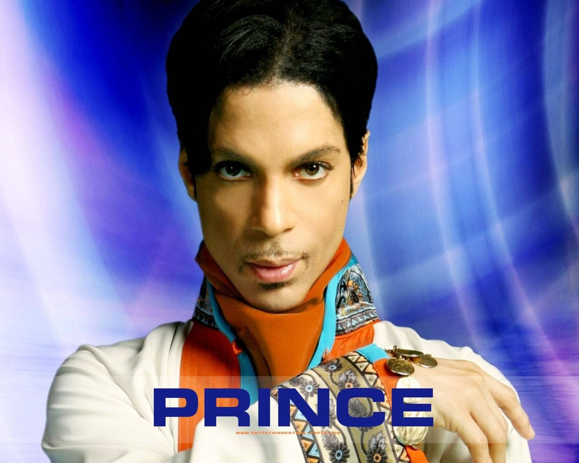 Prince 桌布 壁紙 — Prince 在旋轉的藍色和紫色抽象背景前，穿著華麗的橙色和圖案服裝，強烈地凝視著觀眾。