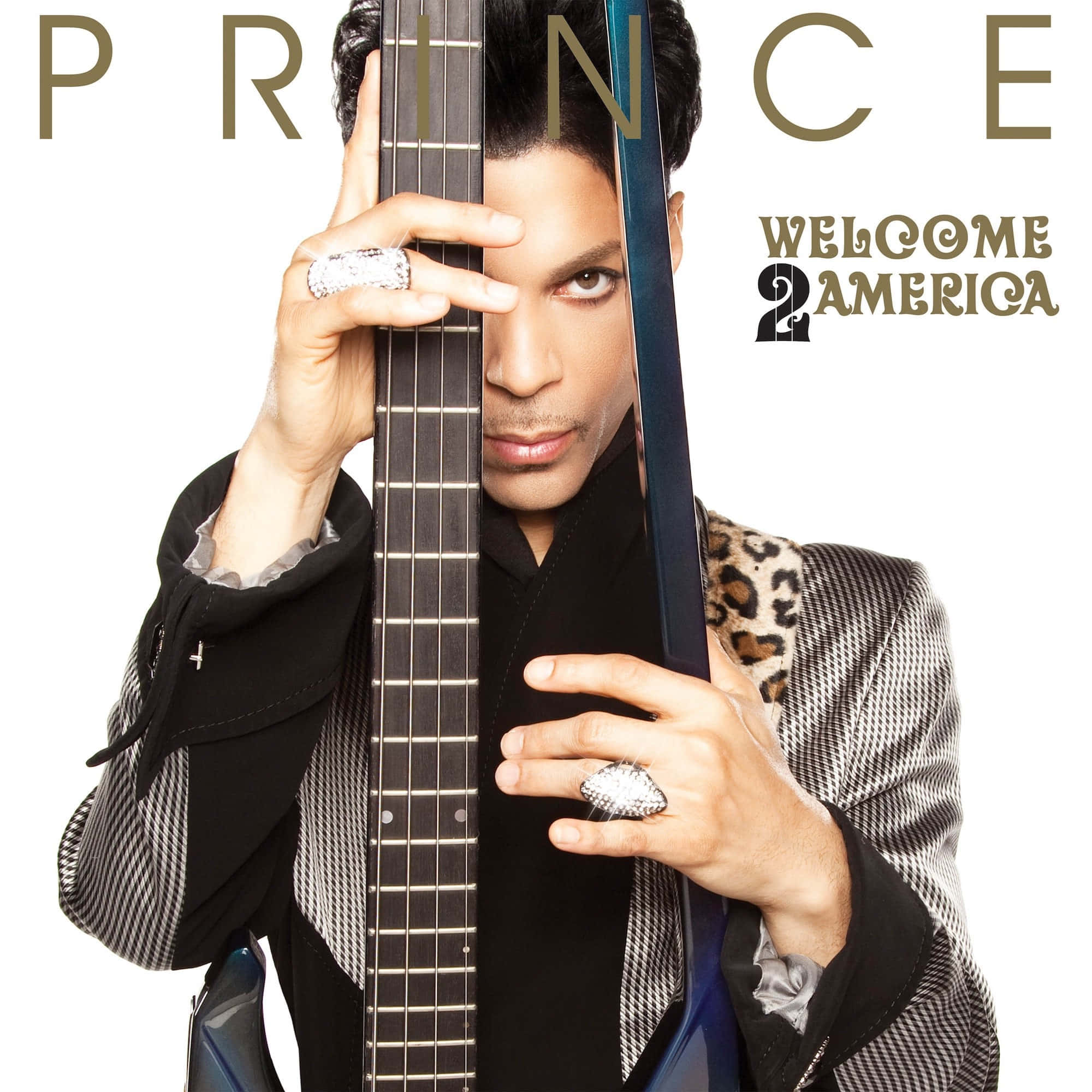 王子 桌布 壁紙 — Prince 垂直握住低音吉他，部分遮蓋他的臉，穿著圖案外套和戒指，背景為白色。