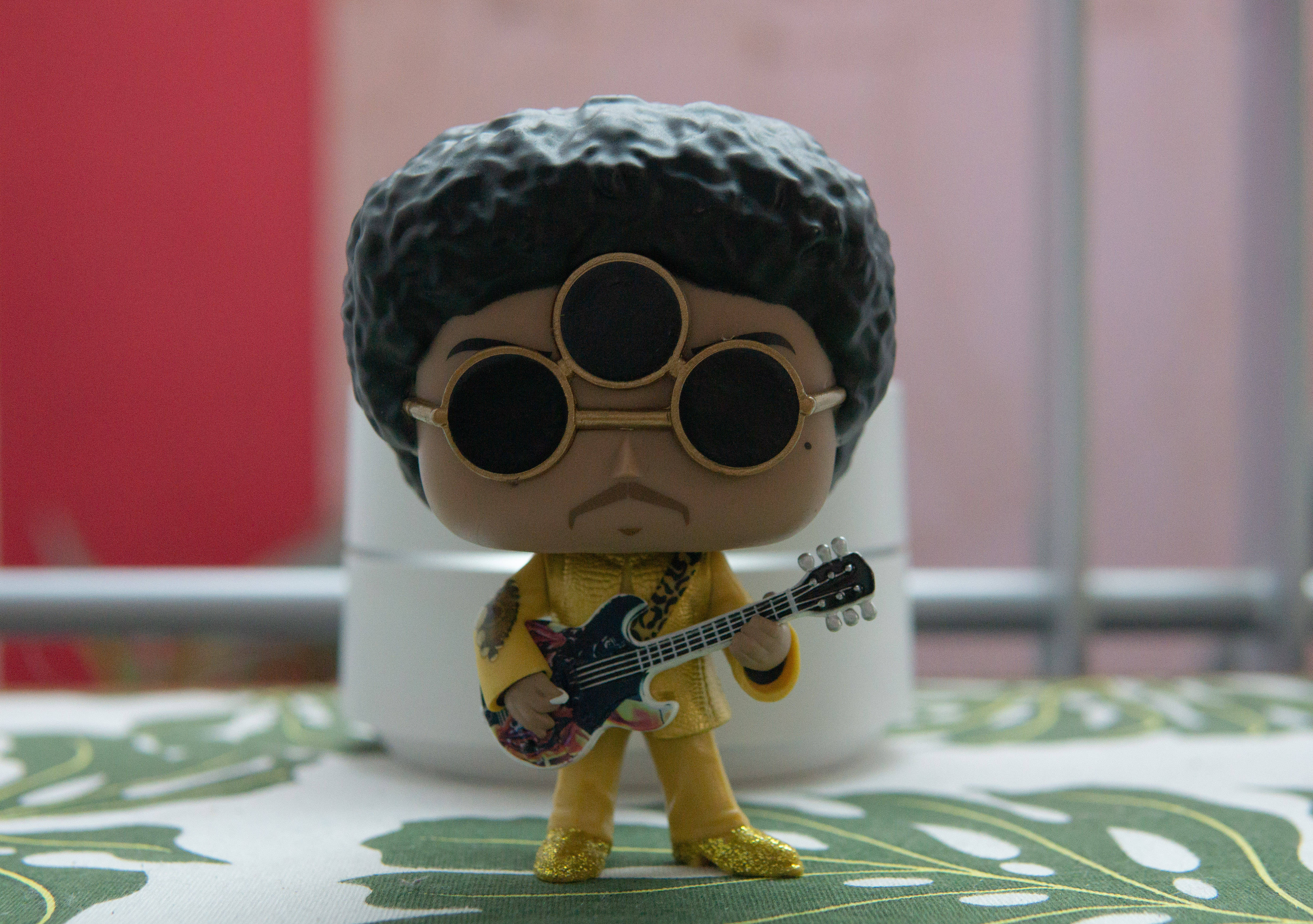 pop 桌布 壁紙 — Prince 的 Funko Pop! 人偶，身穿金色服裝和太陽眼鏡，在葉子圖案的桌子上拿著吉他。