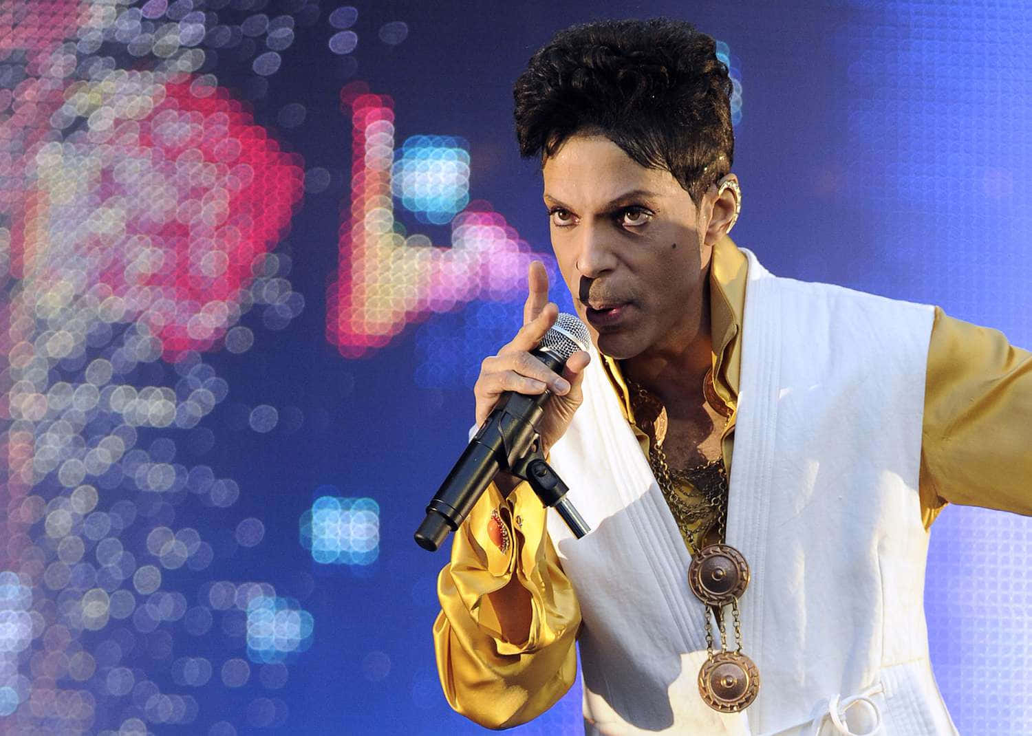 Prince 桌布 壁紙 — Prince 穿著白色背心和金色襯衫，在充滿活力的像素背景前表演。