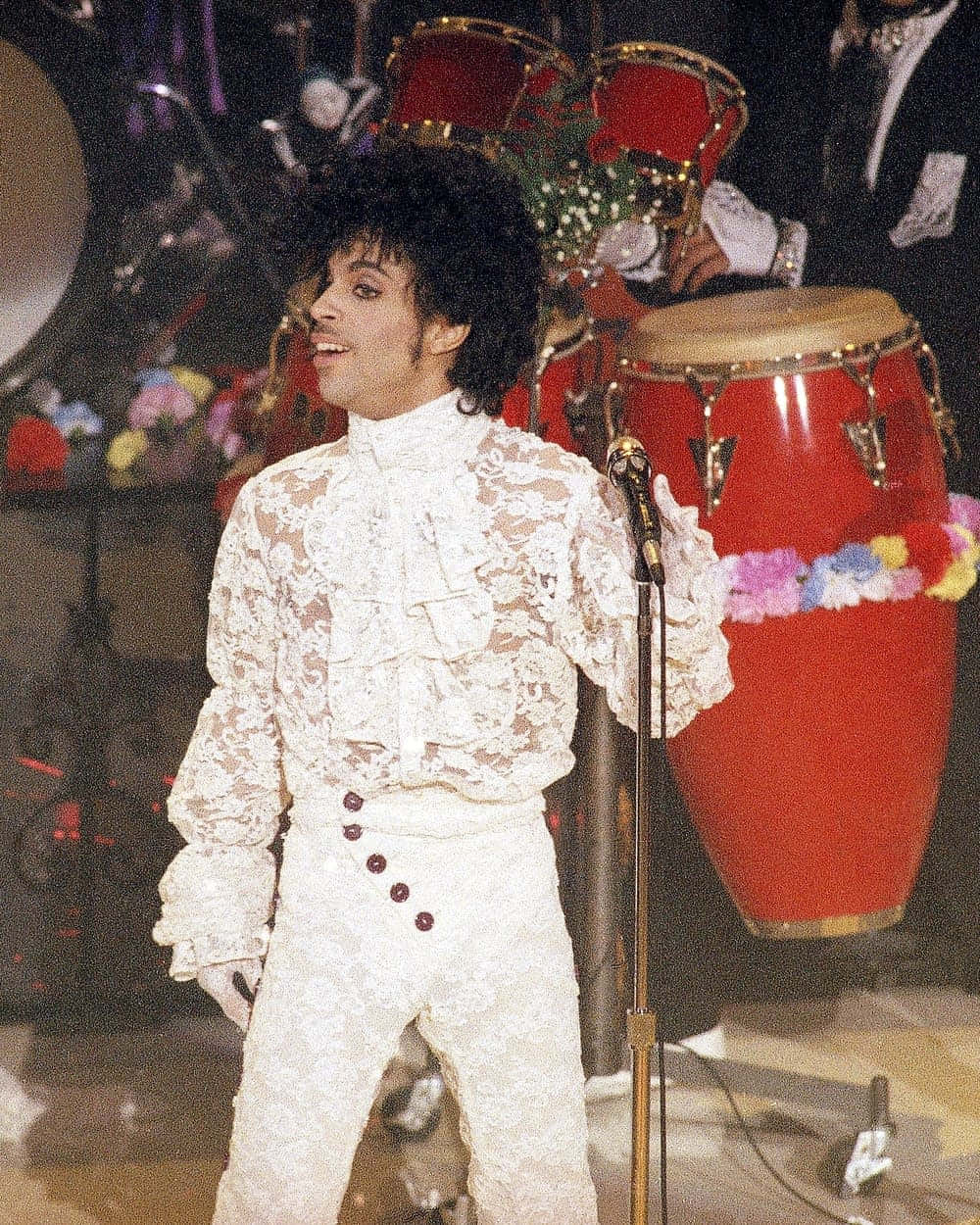 王子 桌布 壁紙 — Prince 穿著白色蕾絲服裝在舞台上表演，身後有紅色鼓。