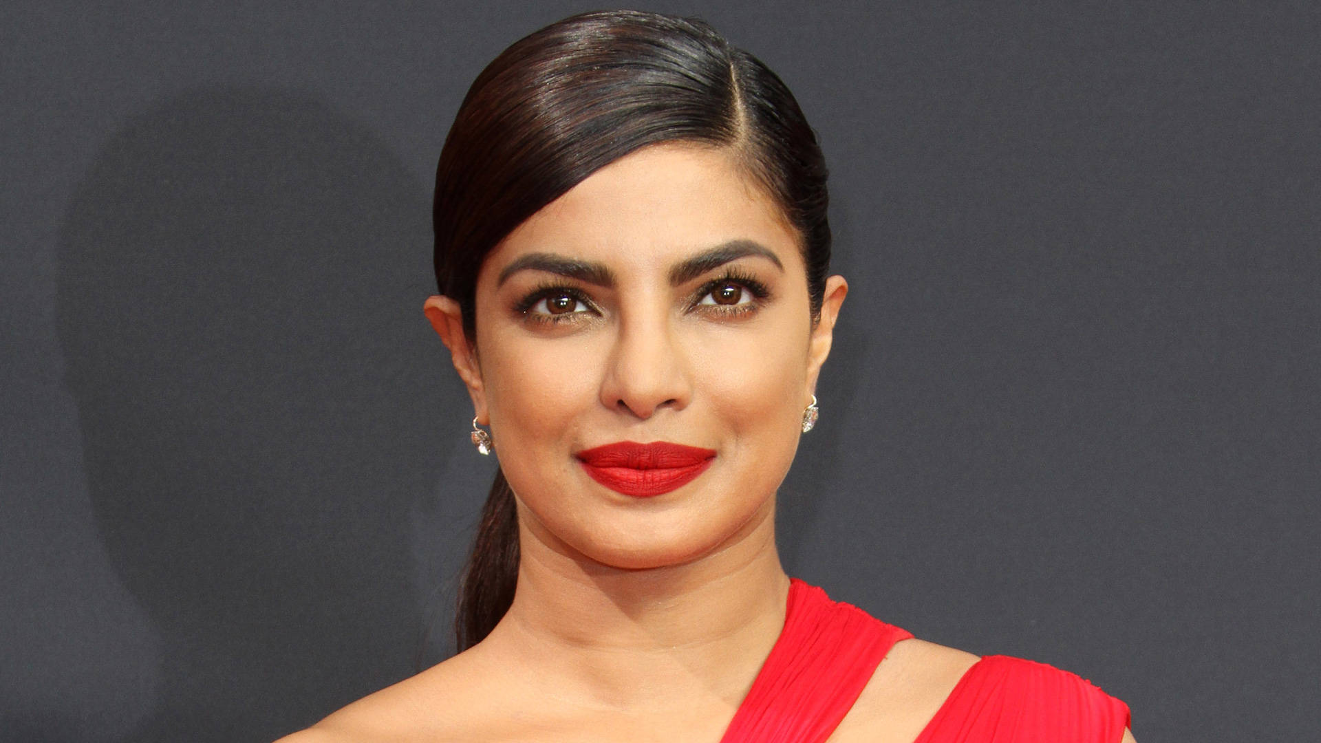 Priyanka 桌布 壁紙 — Priyanka Chopra 在深灰色背景前自信微笑，穿著一件大膽的紅色連衣裙。
