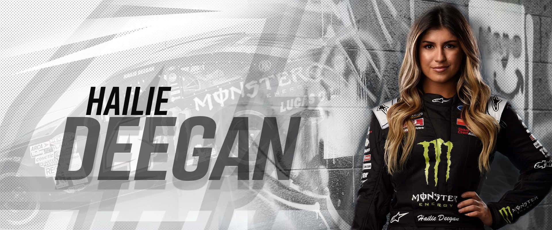  壁紙 — 職業賽車手 Hailie Deegan 穿著她的 Monster Energy 賽車服，在動態模糊的賽車背景前自信地擺姿勢。