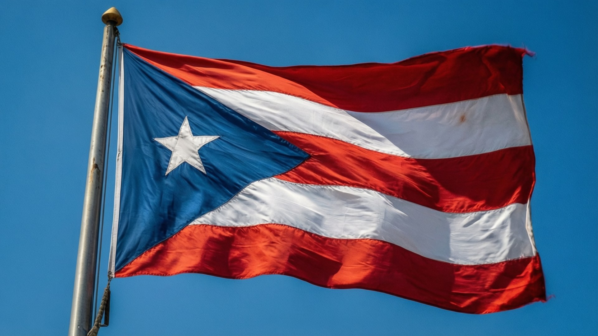 Flag of Puerto Rico Waving 壁紙 — 波多黎各國旗，帶有紅、白、藍條紋和一顆白色星星，在清澈的藍天下動態飄揚。