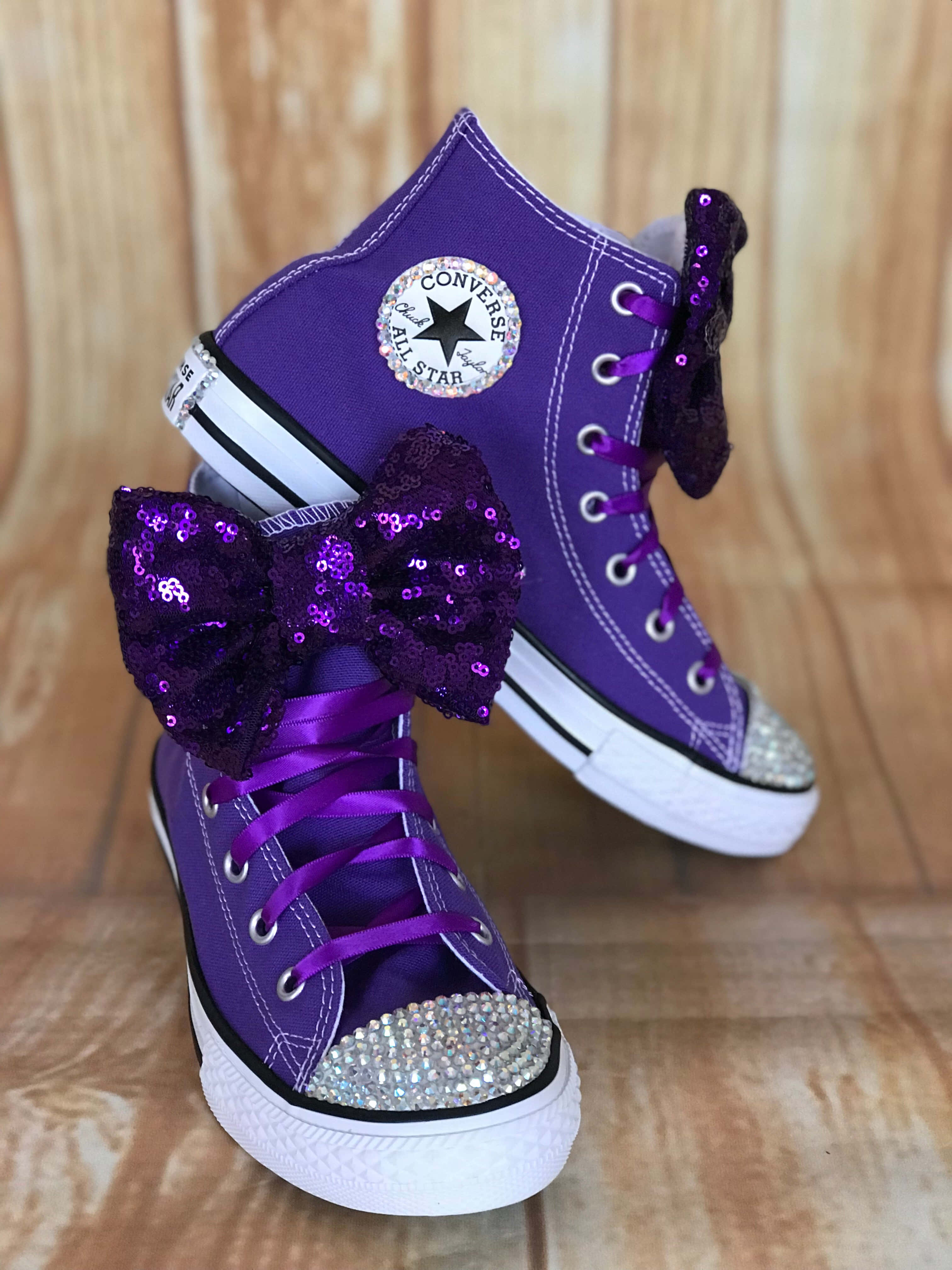 Purple Shoes 桌布 壁紙 — 紫色高筒Converse運動鞋飾有閃亮蝴蝶結和水鑽鞋頭，放在木地板上。