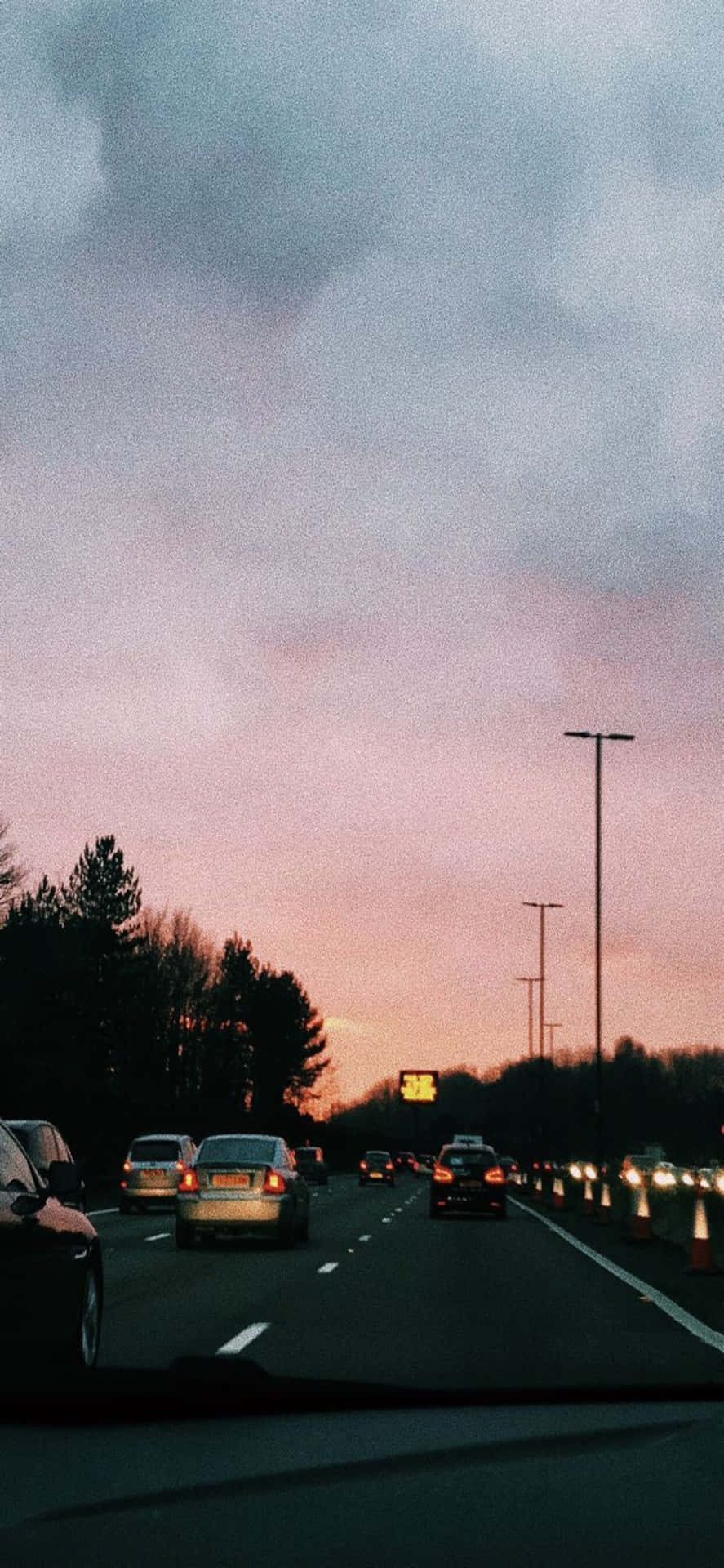 黃昏時分高速公路上的汽車，粉紅和紫色的天空和烏雲。 — iPhone 13 Pro Max 壁紙