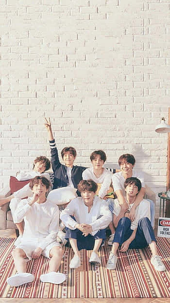 七位身穿白色衣服的年輕男性在室內有圖案的地毯上一起擺姿勢。 — Bts 壁紙