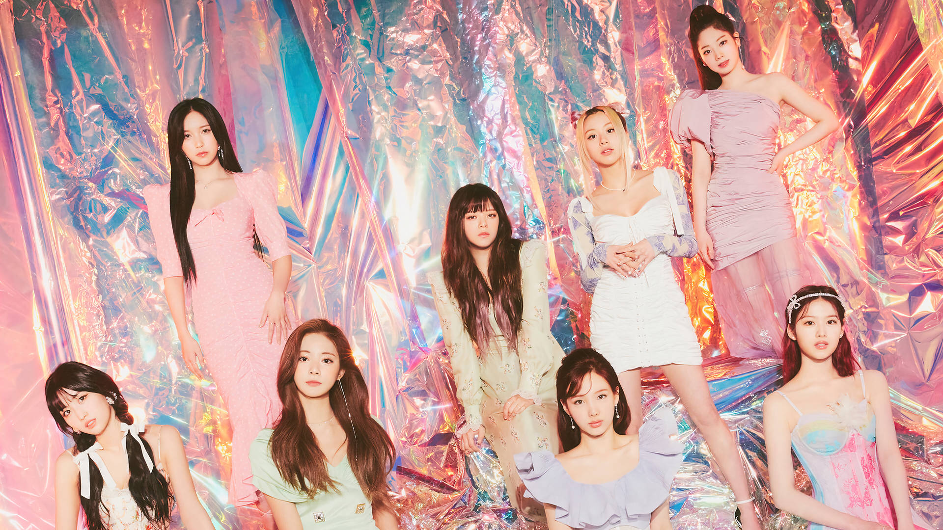 七位身穿粉彩服裝的時尚女性在閃亮的箔紙背景前擺姿勢。 — Twice 壁紙