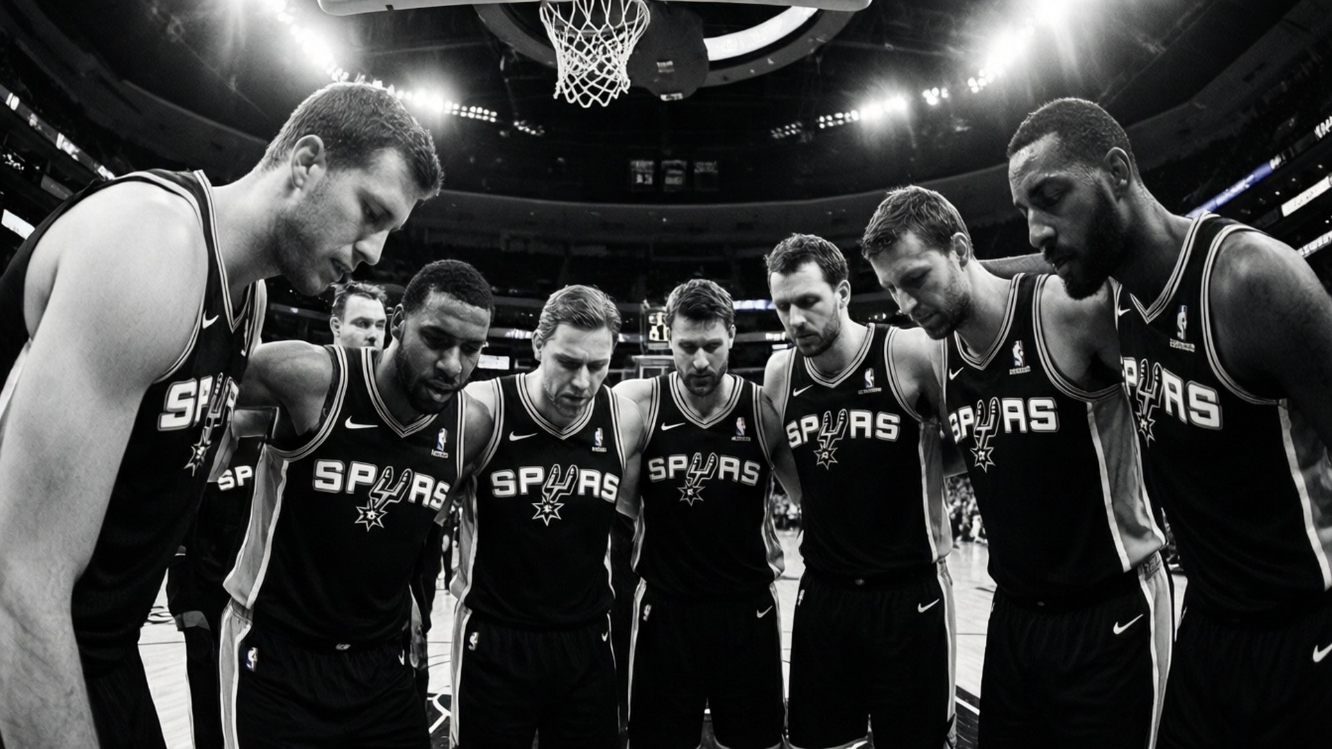 Spurs Team Huddle 壁紙 — 七位聖安東尼奧馬刺籃球運動員在球場燈光下的黑白照片中圍成一圈，上方有籃框。