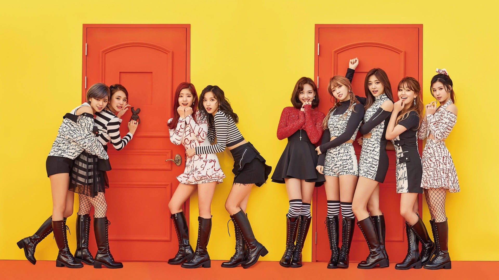 七位穿著時尚服裝的K-pop女孩在紅色門和黃色牆前擺姿勢。 — Twice 壁紙