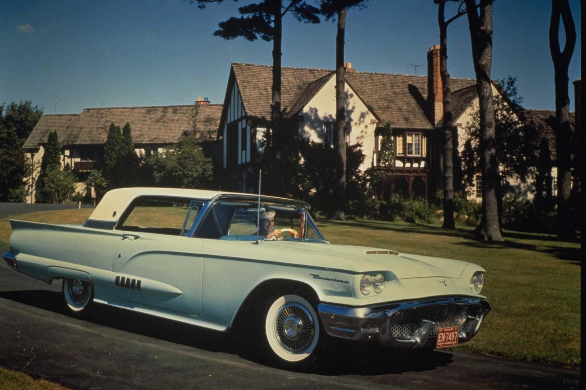 Ford Thunderbird 桌布 壁紙 — 一輛淺藍色1950年代Thunderbird敞篷車停泊在都鐸式房屋前的車道上，周圍有樹木和晴朗的藍天。