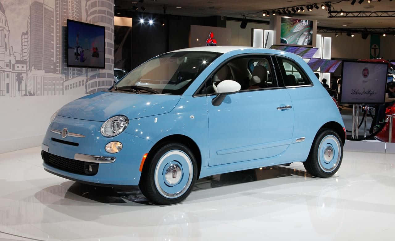 Fiat 500 桌布 壁紙 — 一輛淺藍色Fiat 500配白色輪胎，在展廳燈光下於反光地板上閃閃發光。